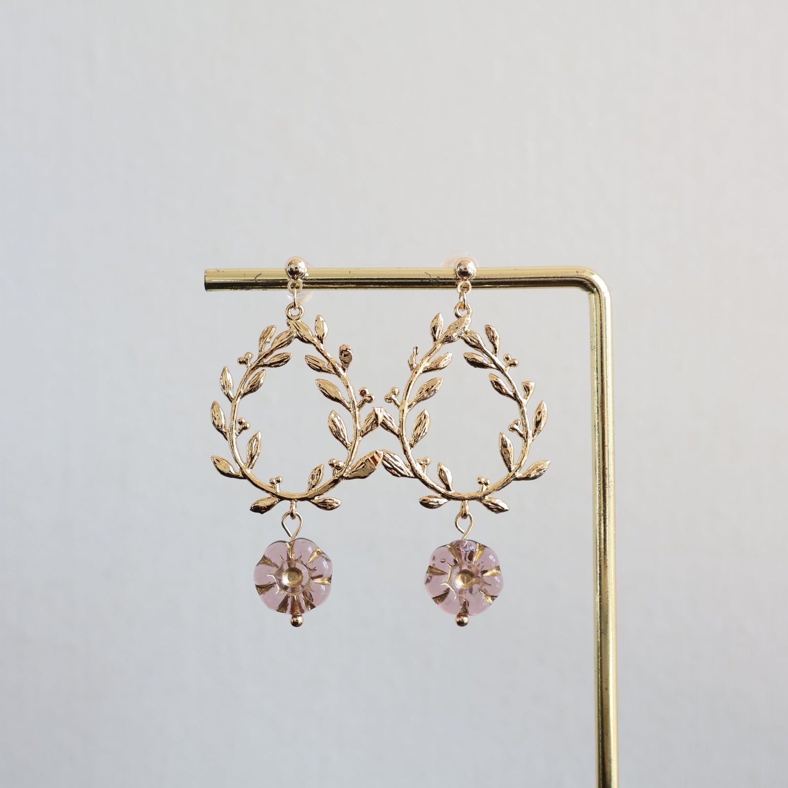 Gold leaf earrings with pink gemstones on a gold stand against a light gray background