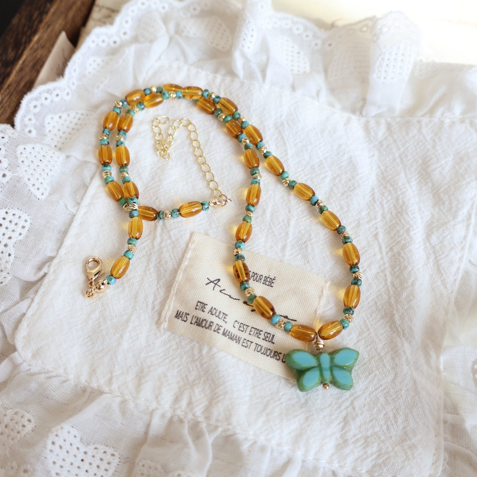 Beaded necklace with a butterfly charm on a white lace fabric background