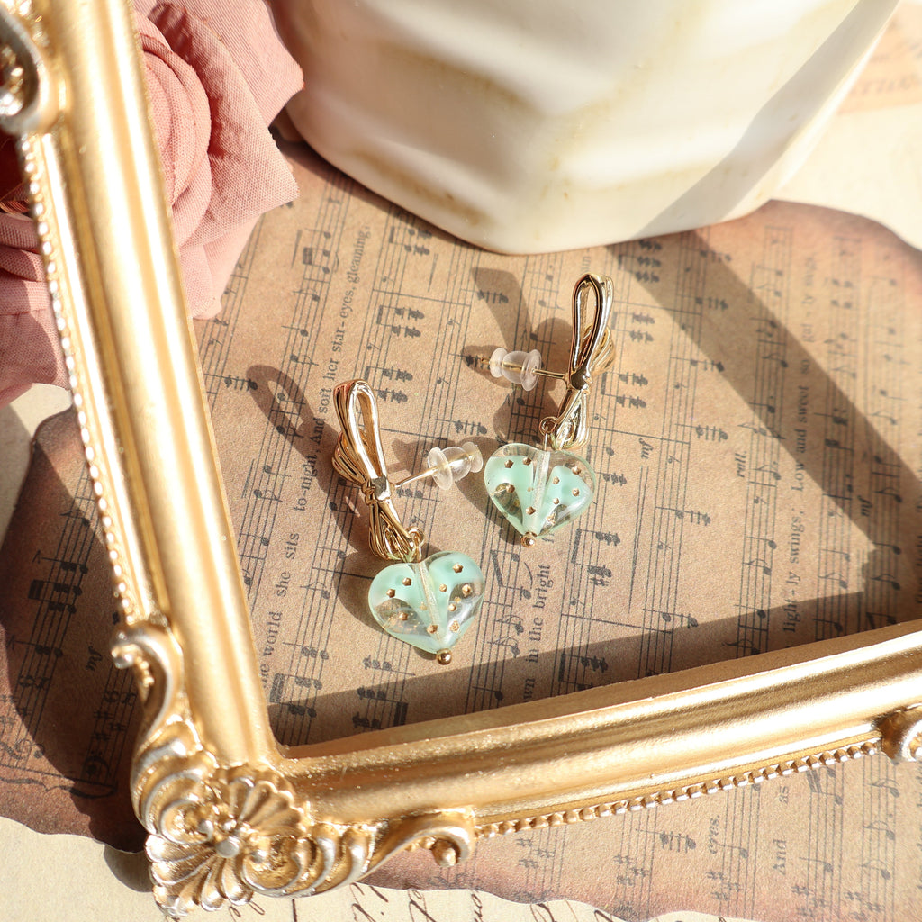 Pair of heart-shaped earrings on a gold frame with sheet music underneath