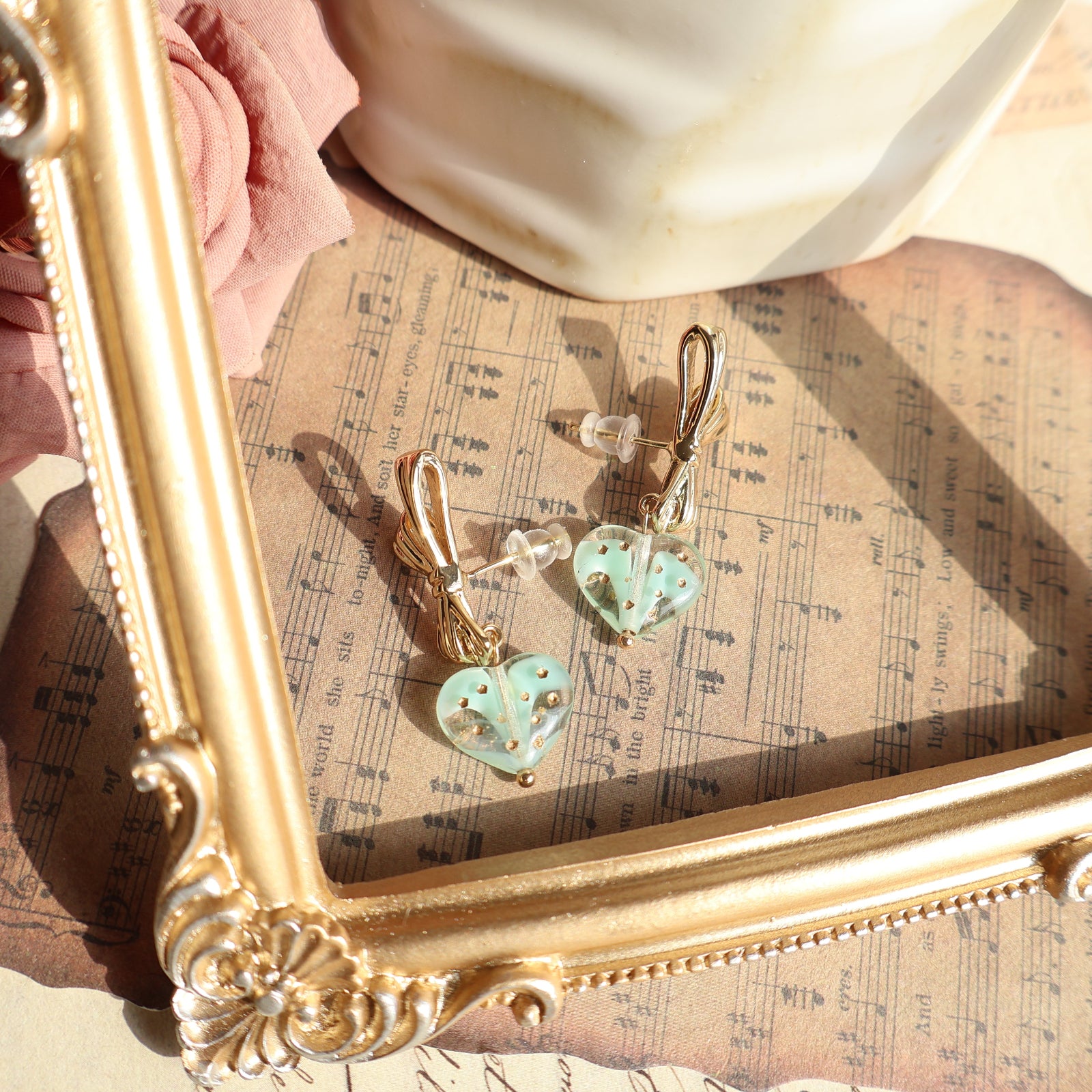 Pair of heart-shaped earrings on a gold frame with sheet music underneath