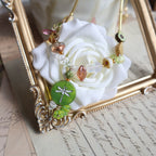 Decorative bracelet with beads and a green charm on a white rose, set against an ornate gold frame.