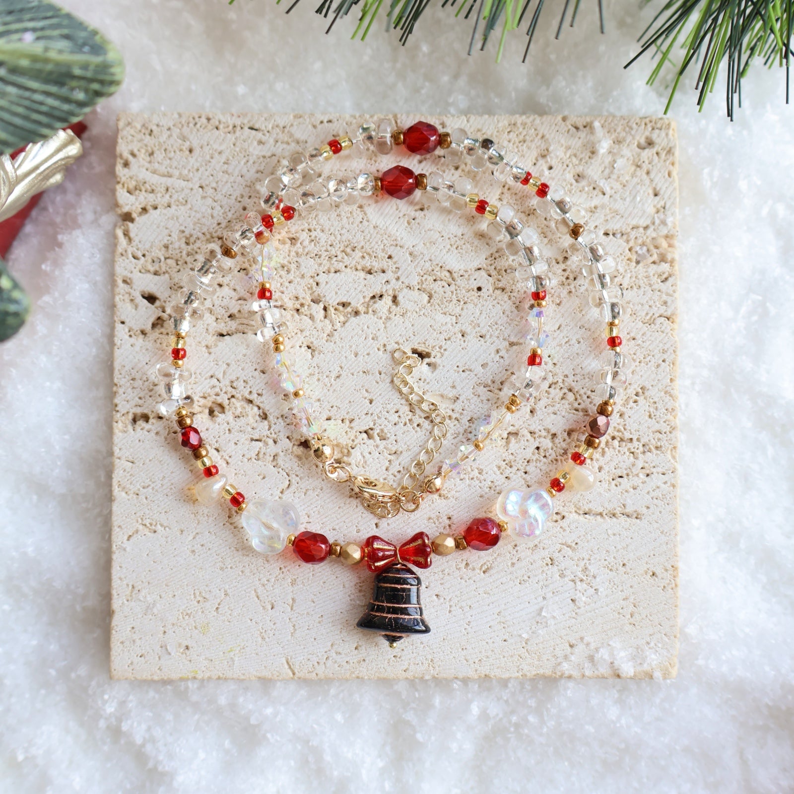 Beaded necklace with a bell pendant on a stone surface with Christmas decorations.