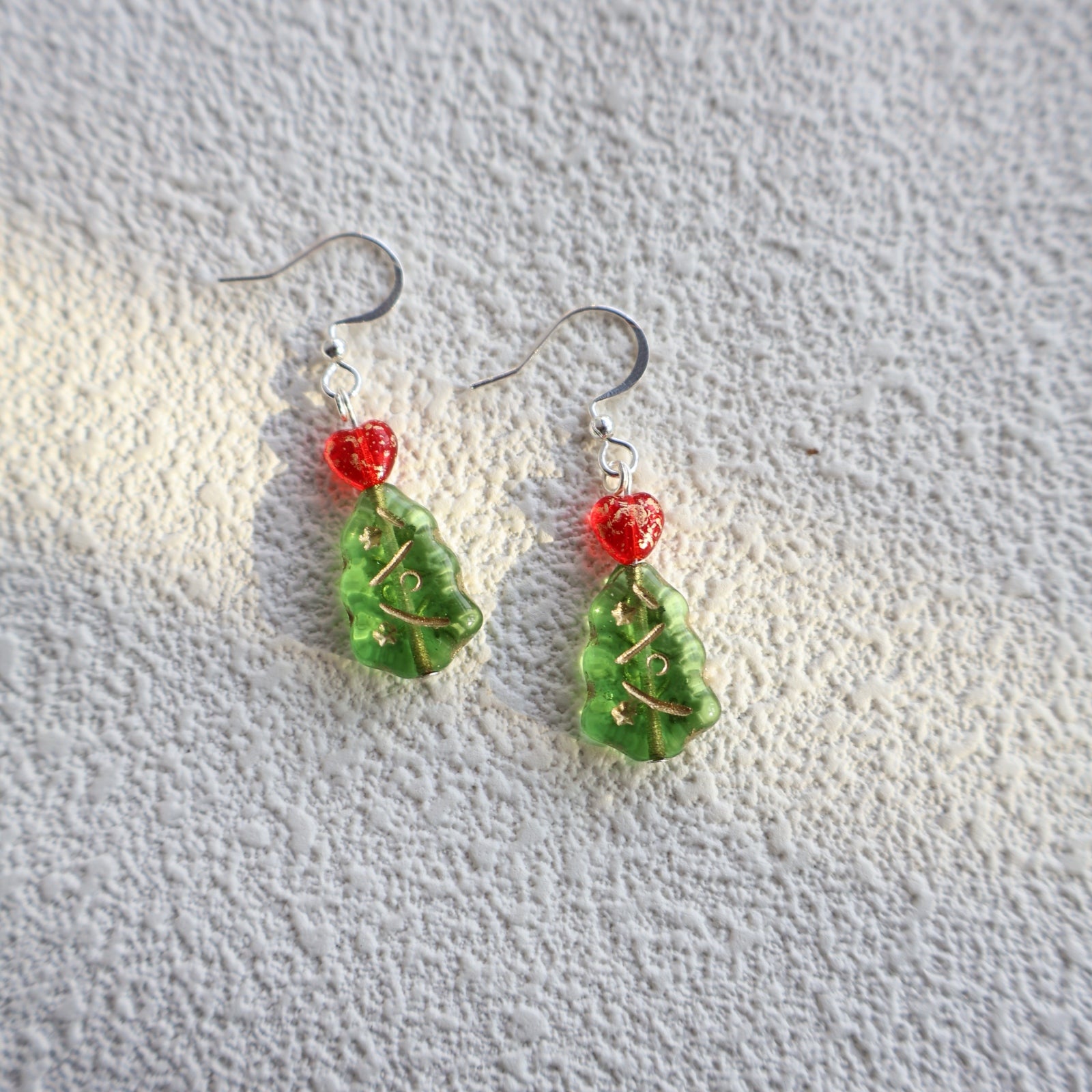 Pair of green Christmas tree-shaped earrings with red berries on a textured white surface.