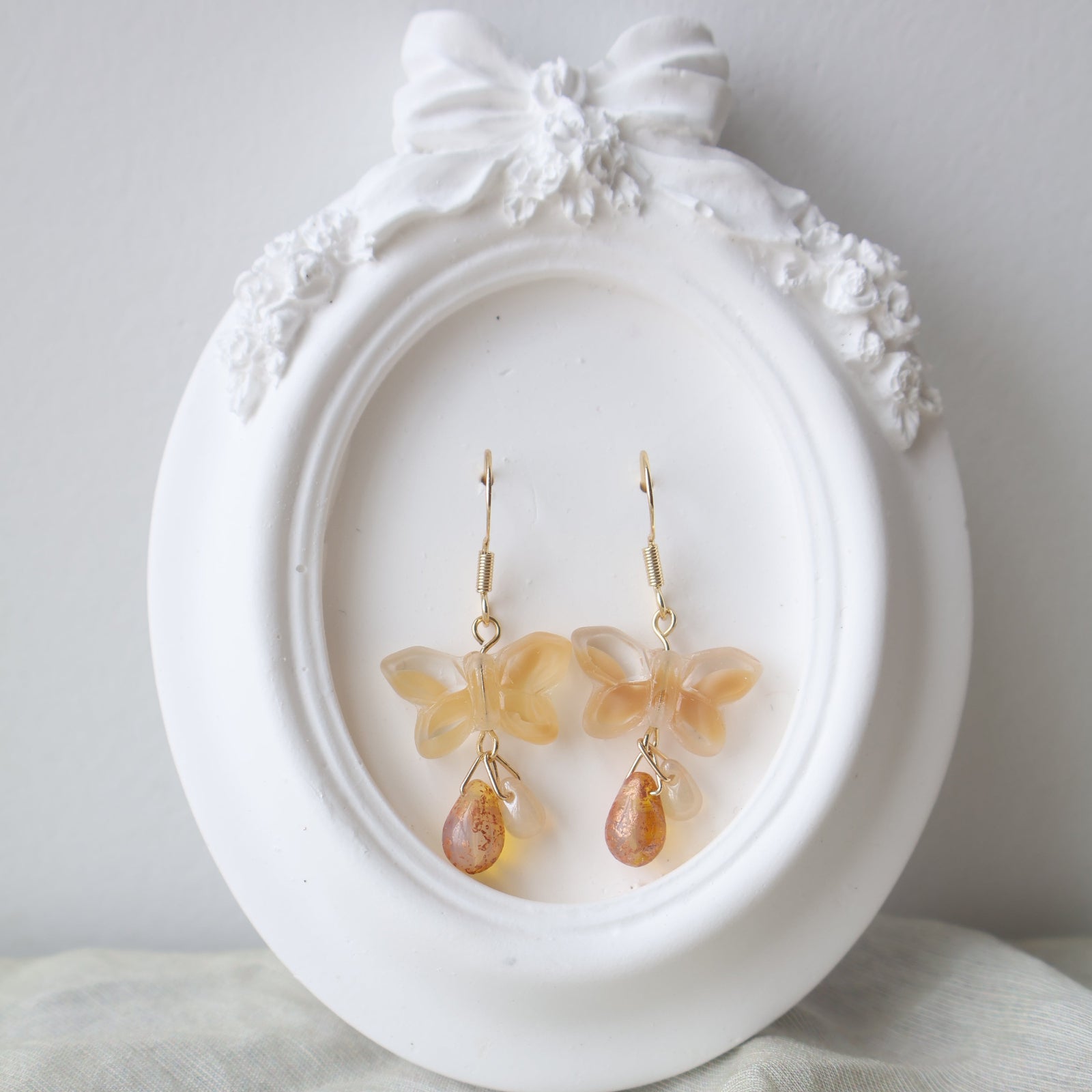 Butterfly-shaped earrings on a decorative white stand with a bow