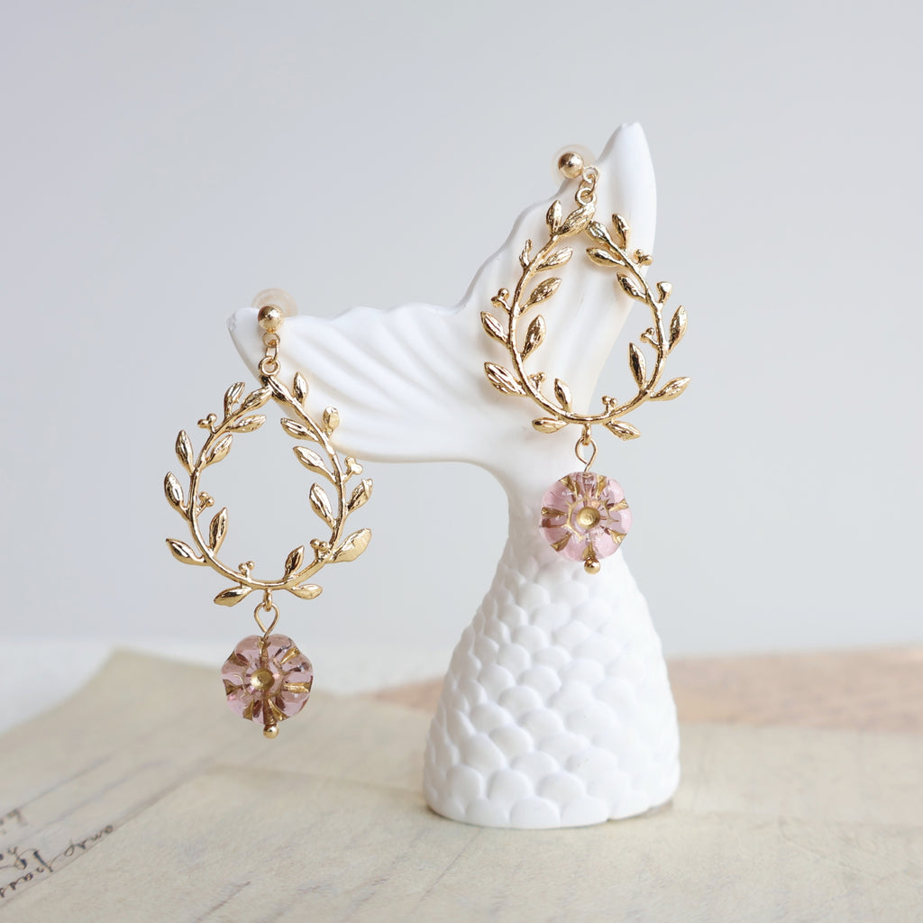 Gold earrings with pink gemstones on a white stand against a light background