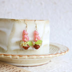 Pair of pink and green beaded earrings on a ceramic plate with a white background