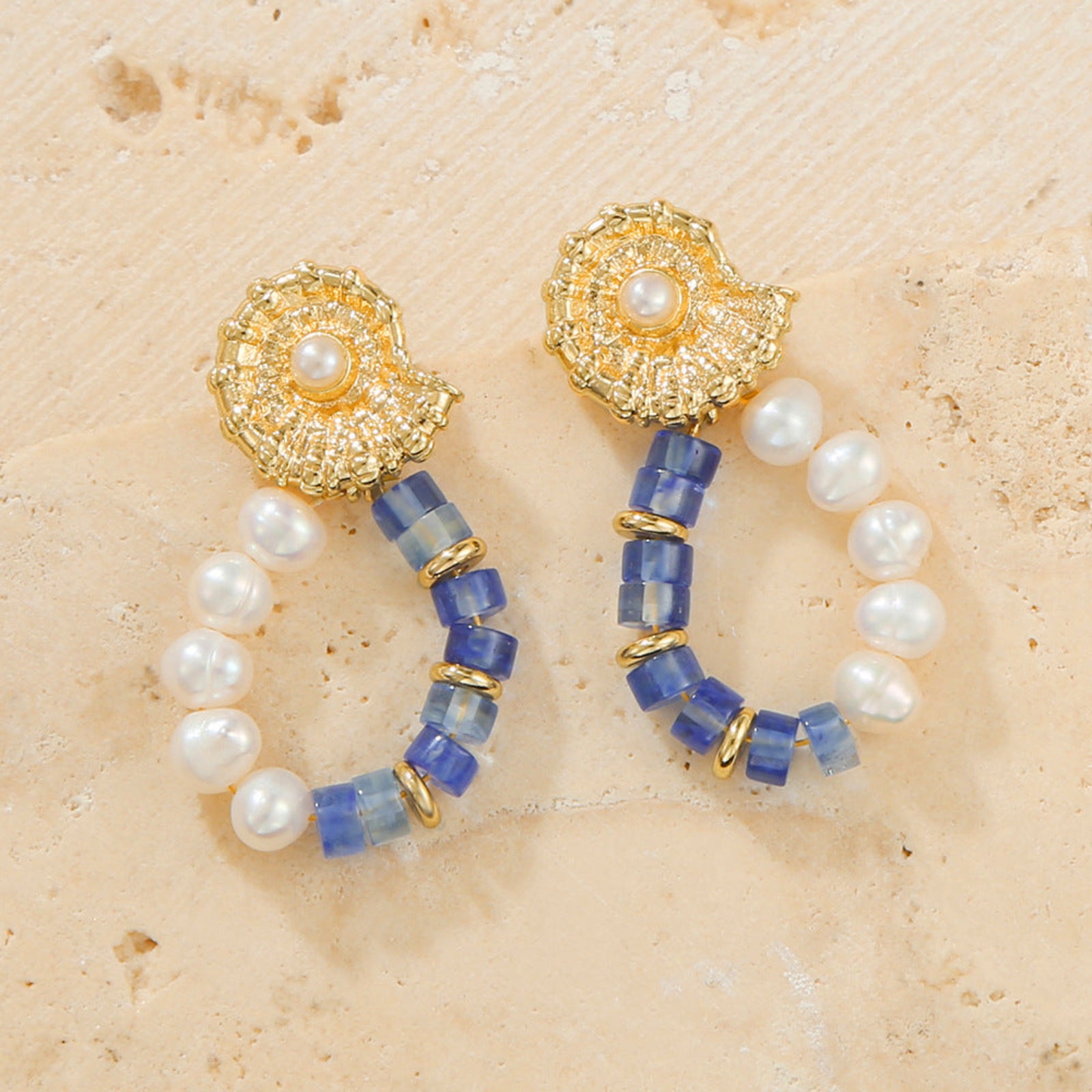 Pair of earrings with gold, blue, and pearl beads on a beige surface