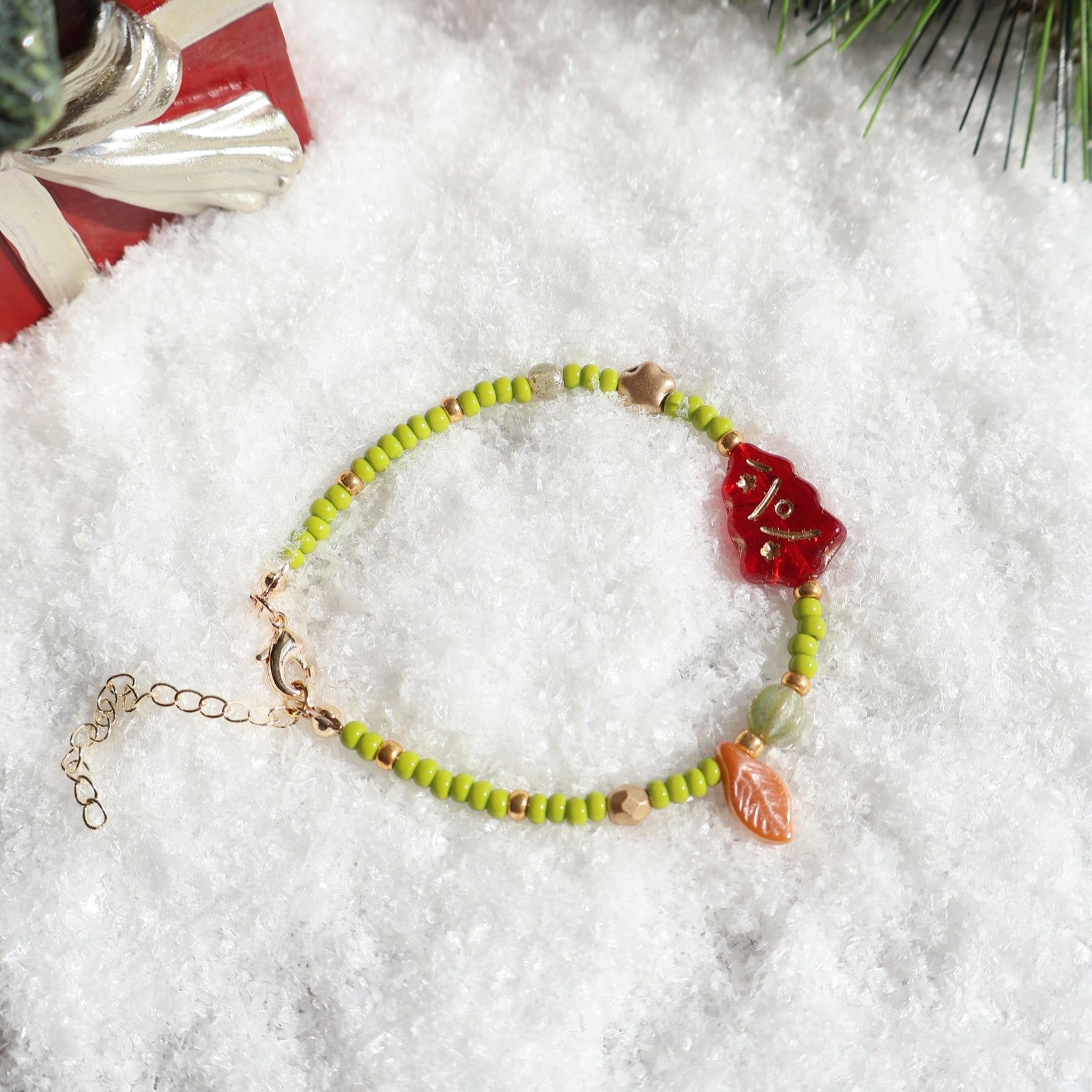Green beaded bracelet with red and gold charms on a snowy background