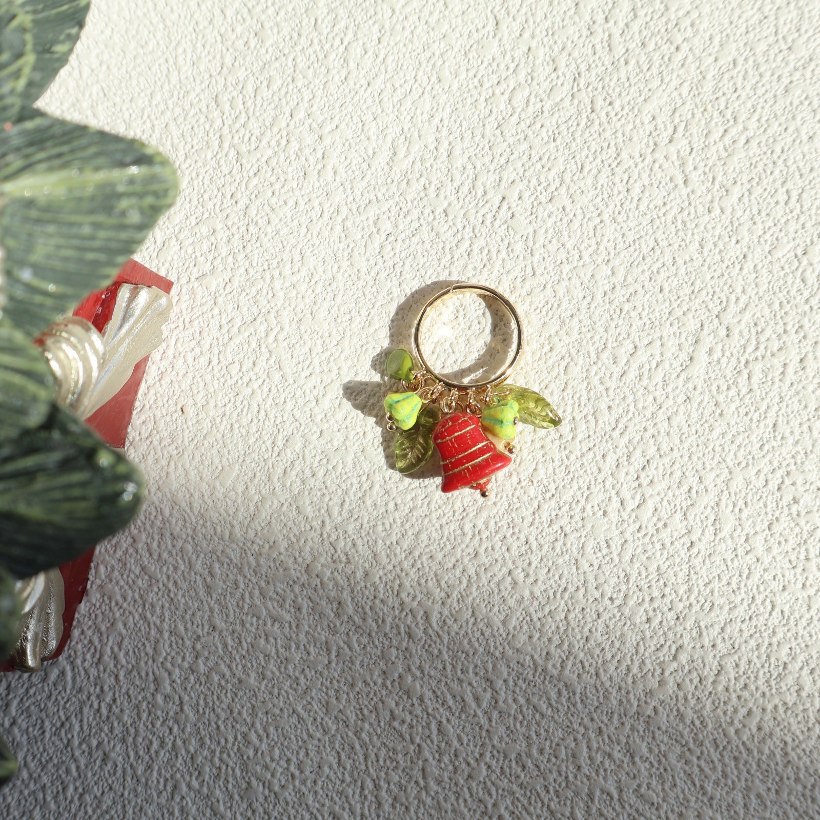 Decorative ring with green leaves and a red bell on a textured white surface