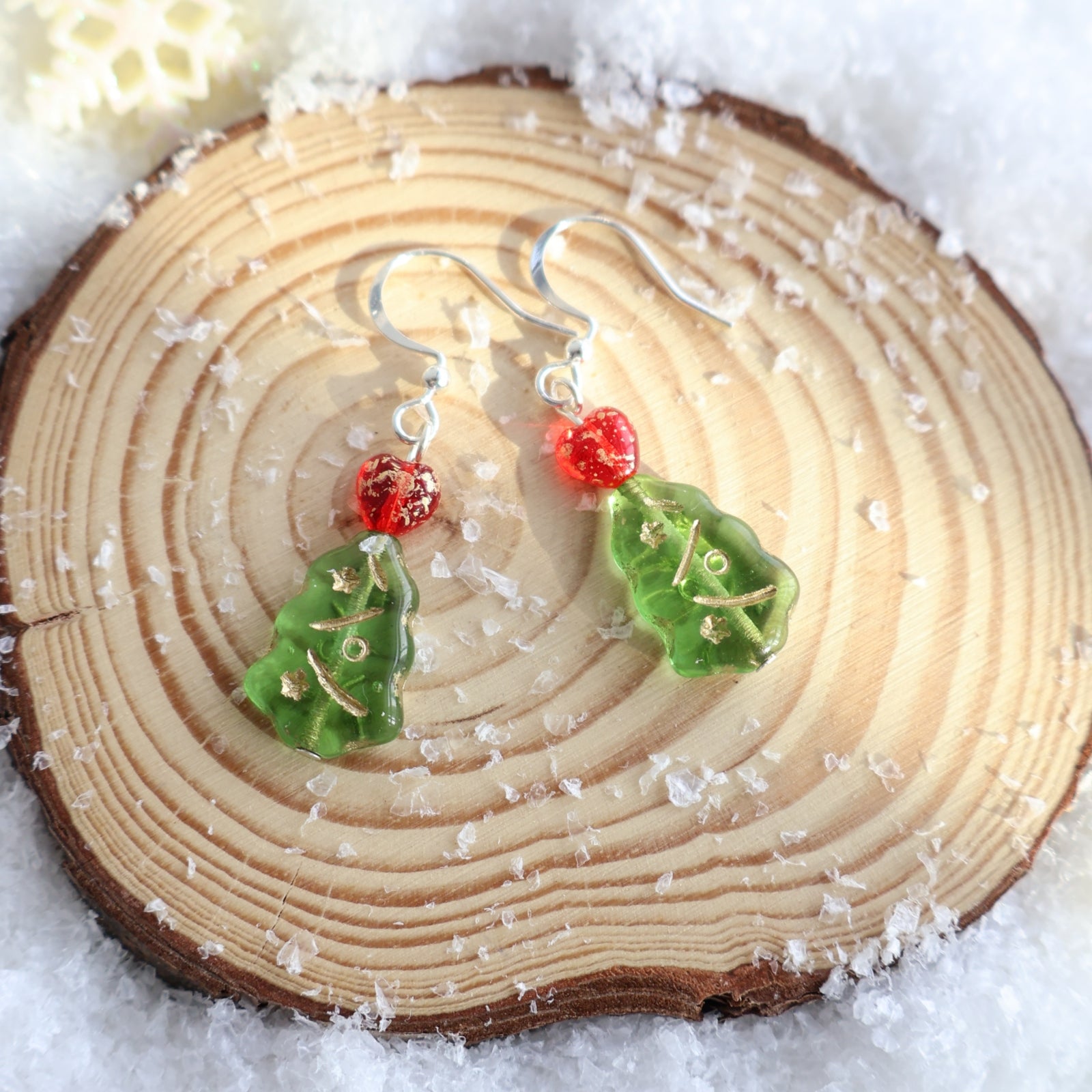 Green leaf-shaped earrings with red centers on a wooden slice.