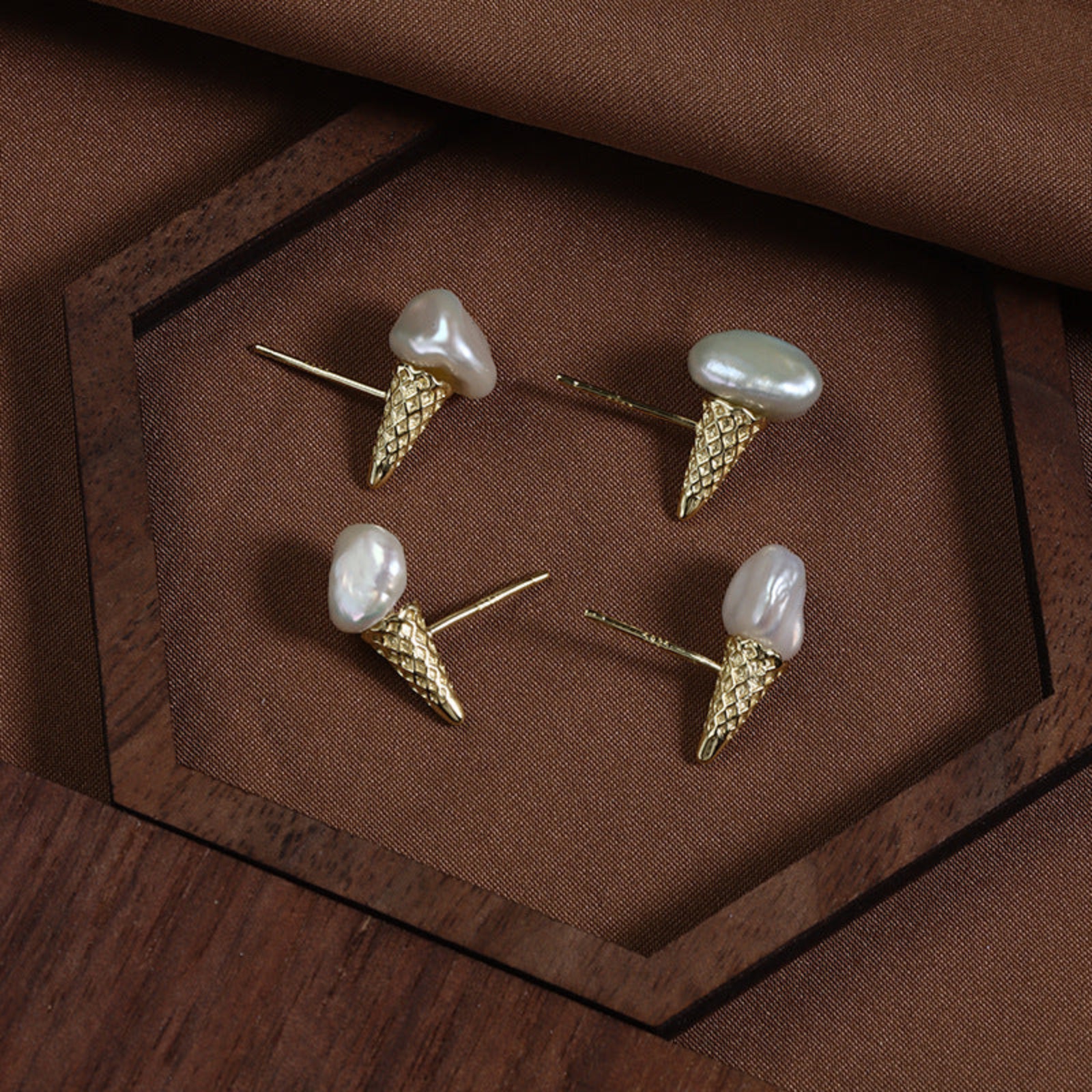 Gold ice cream cone-shaped earrings with pearl tops on a brown fabric background