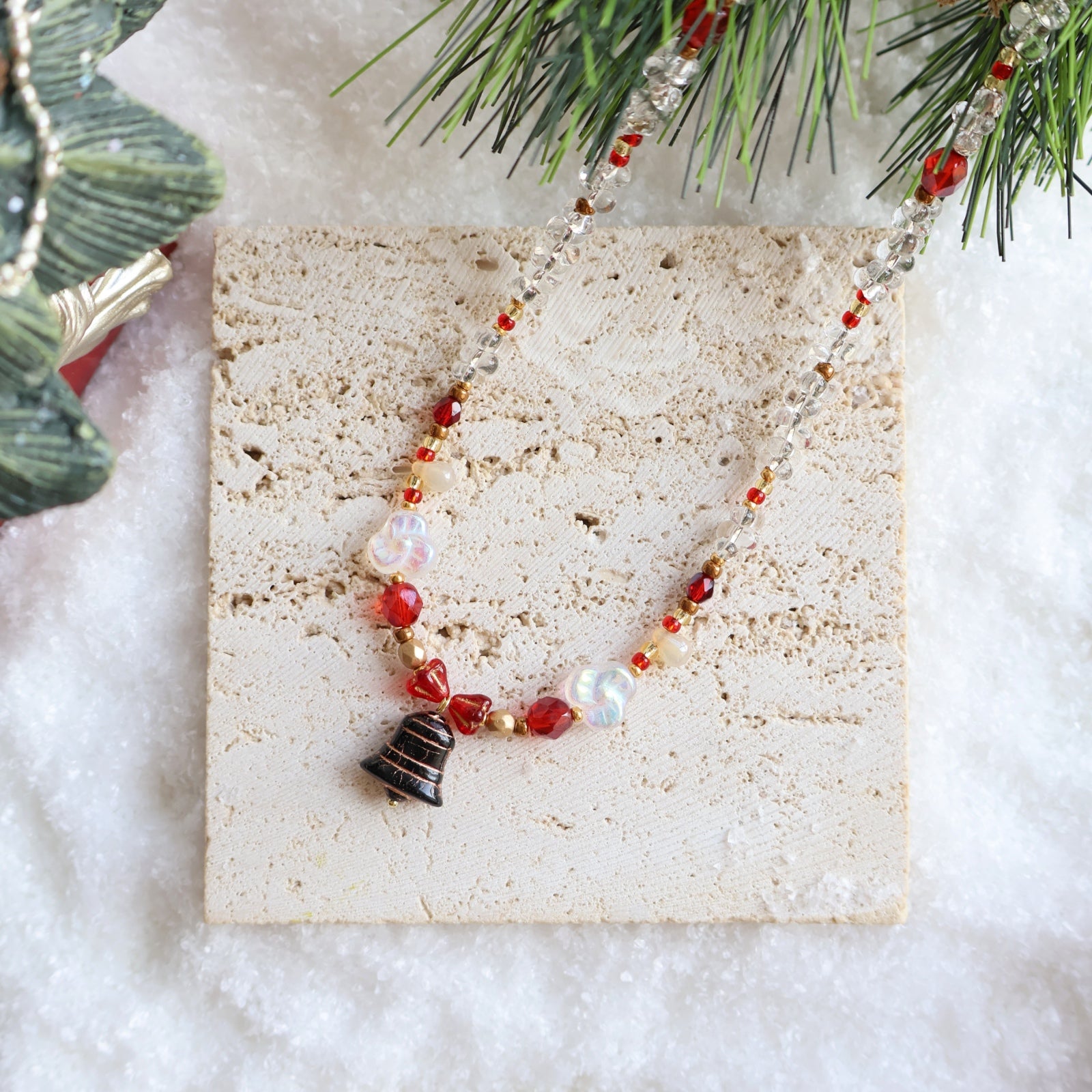 Necklace with red and gold beads on a stone surface with Christmas decorations.