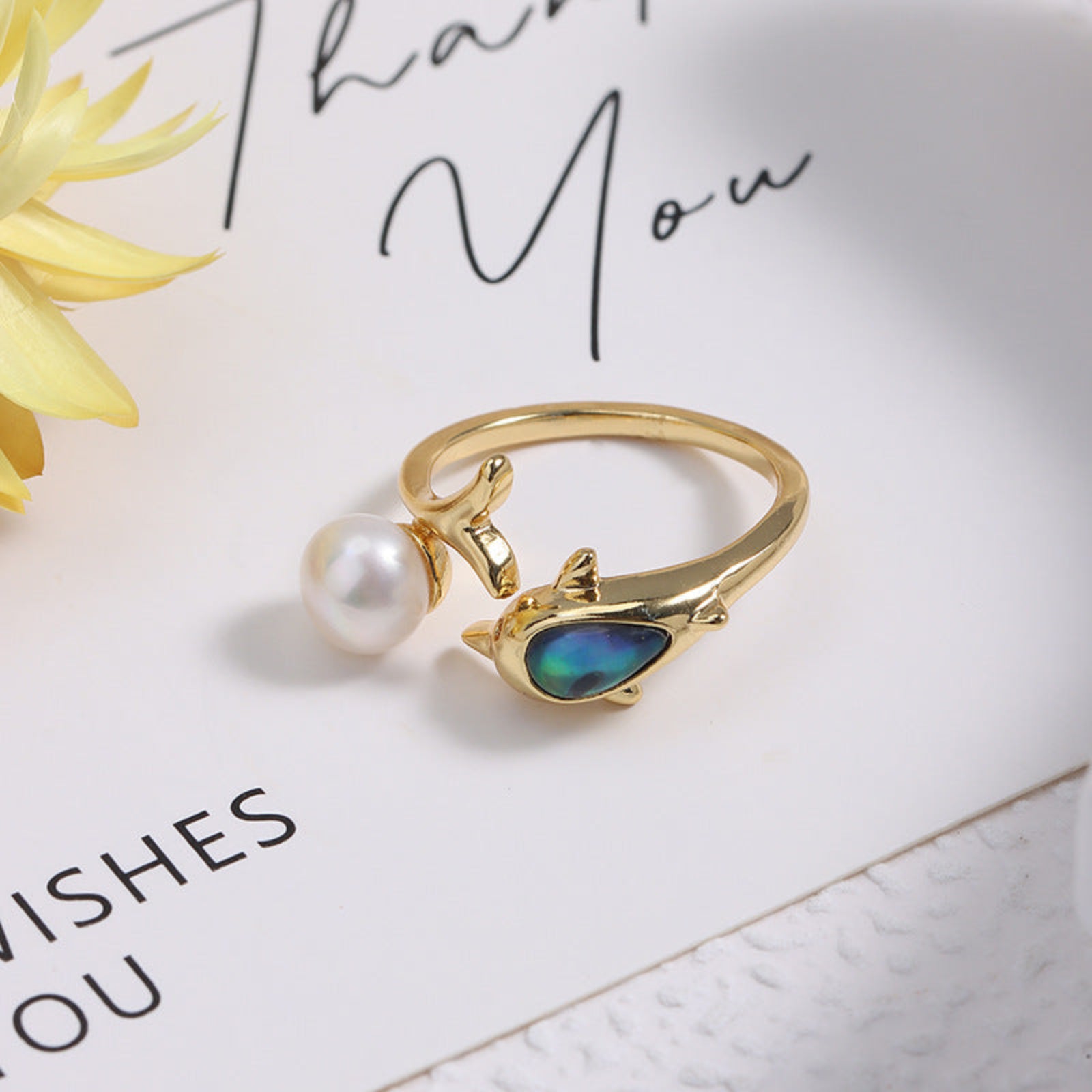 Gold ring with a pearl and colorful stone on a white surface with text