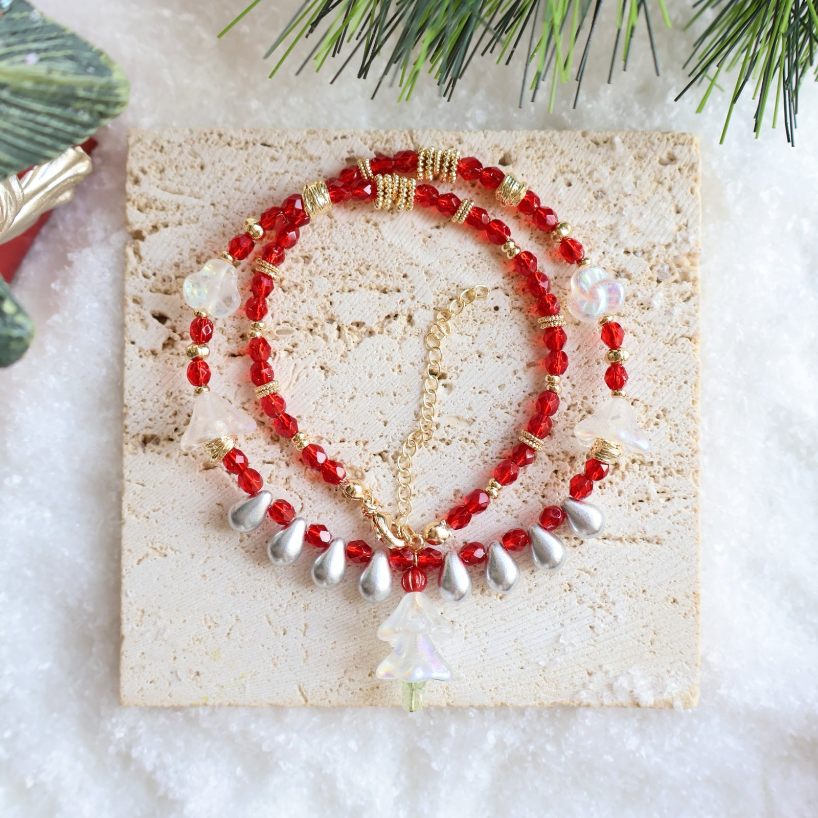 Red and gold beaded necklace on a textured stone surface with greenery in the background