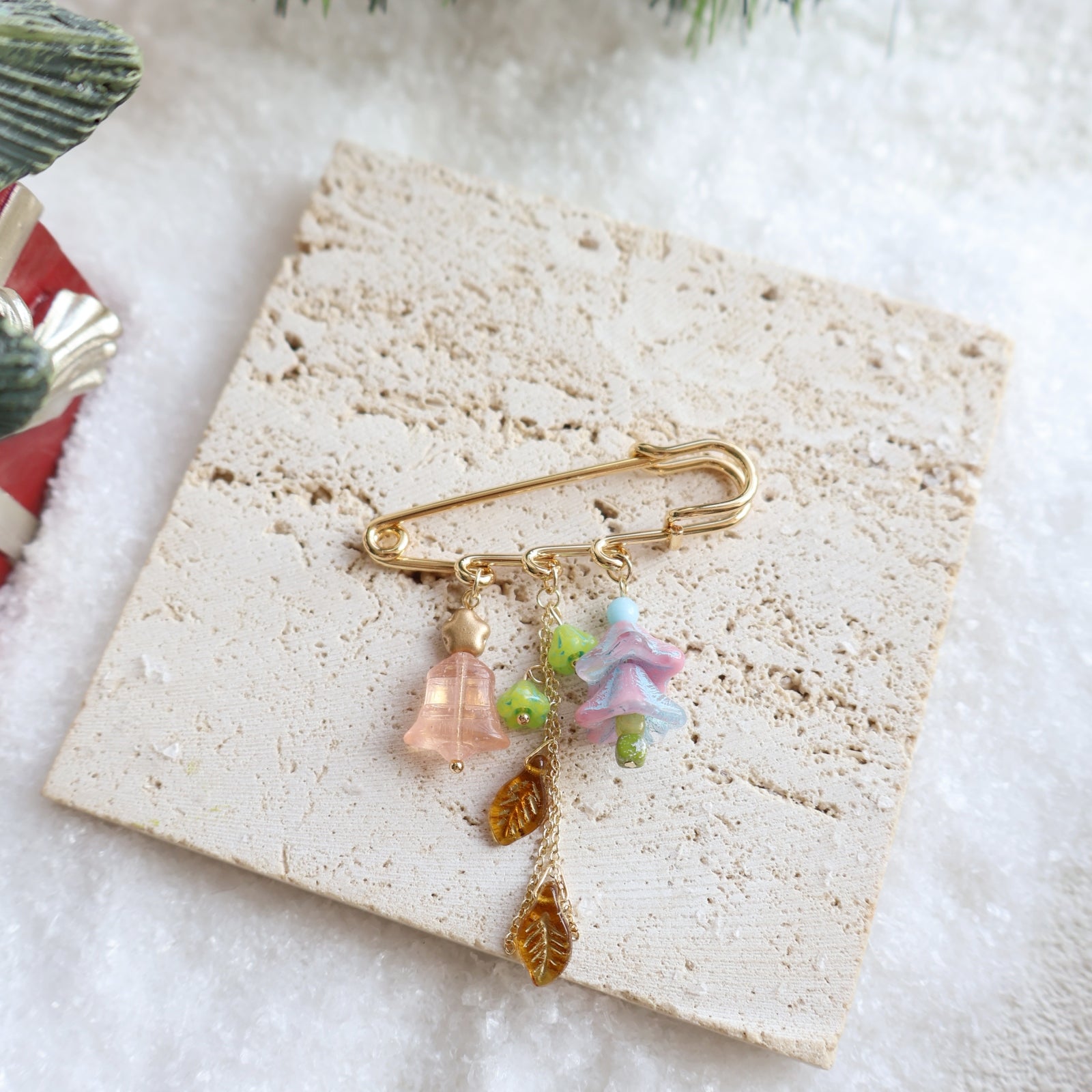 Decorative brooch with floral and leaf charms on a textured stone surface