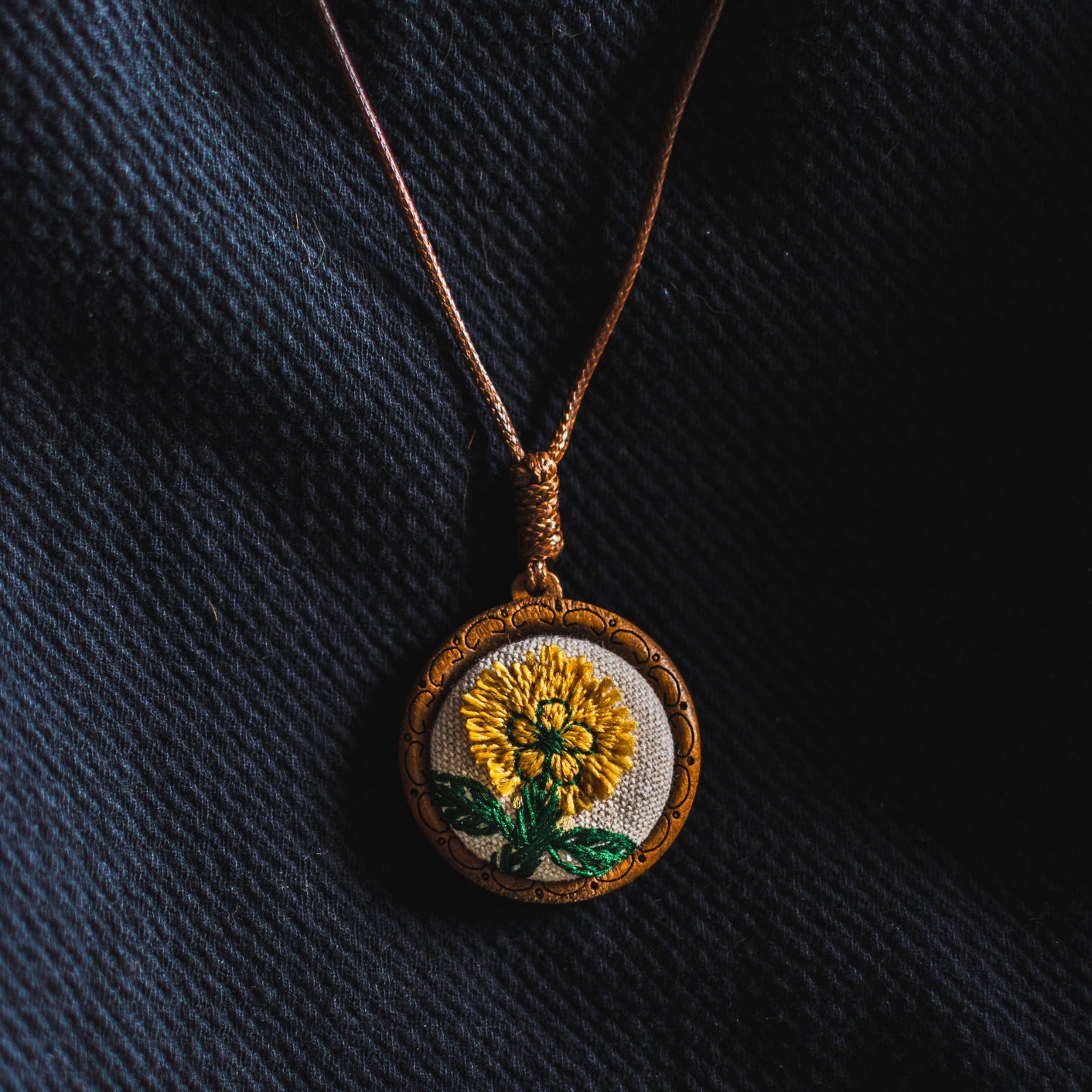 Embroidered pendant with a sunflower design on a dark fabric background