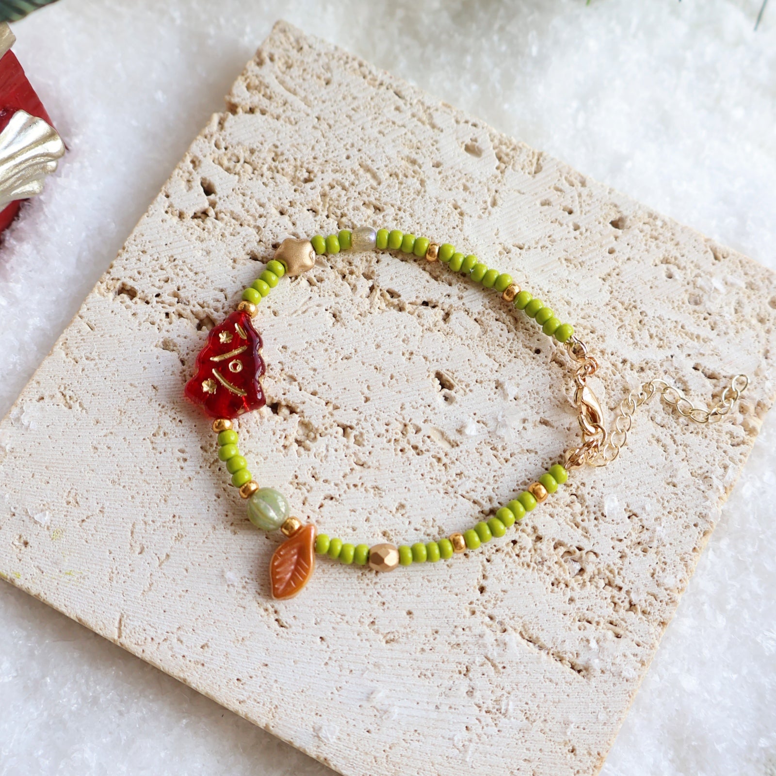 Bracelet with green beads and a red charm on a textured surface