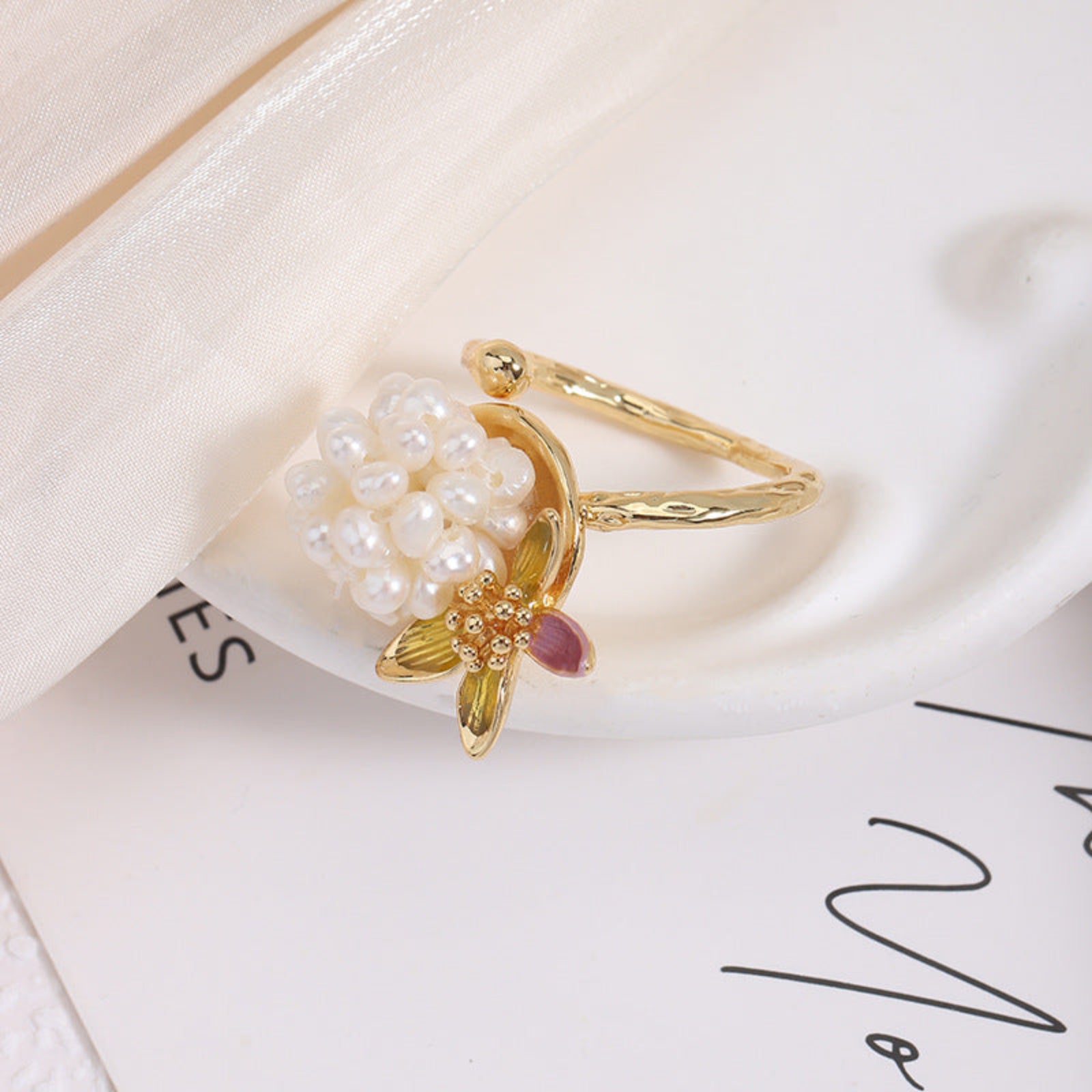 Gold ring with pearl and gemstone design on a white surface