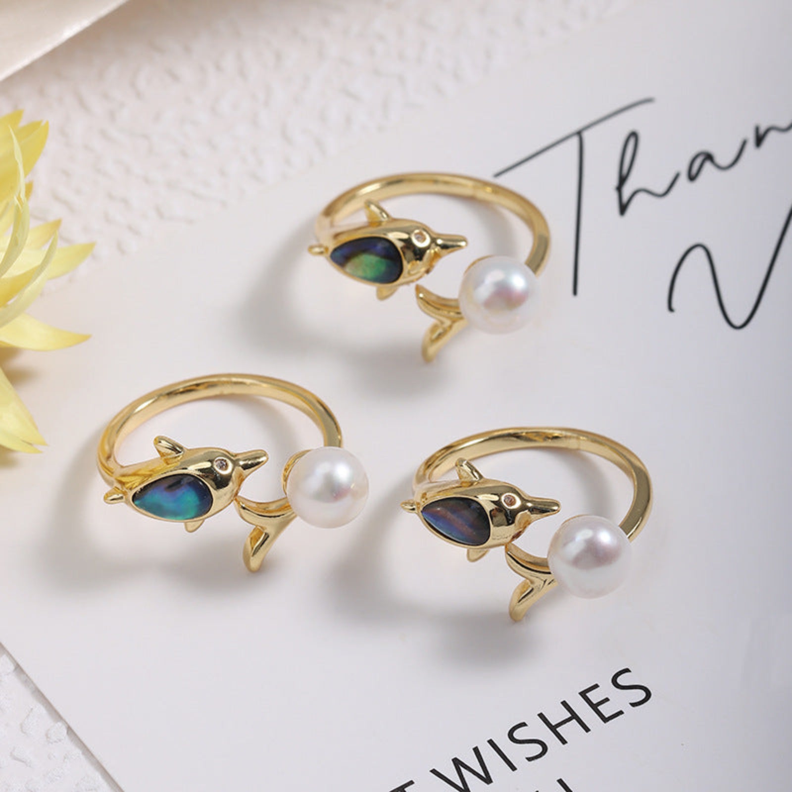 Three gold rings with dolphin designs and pearls on a white surface.
