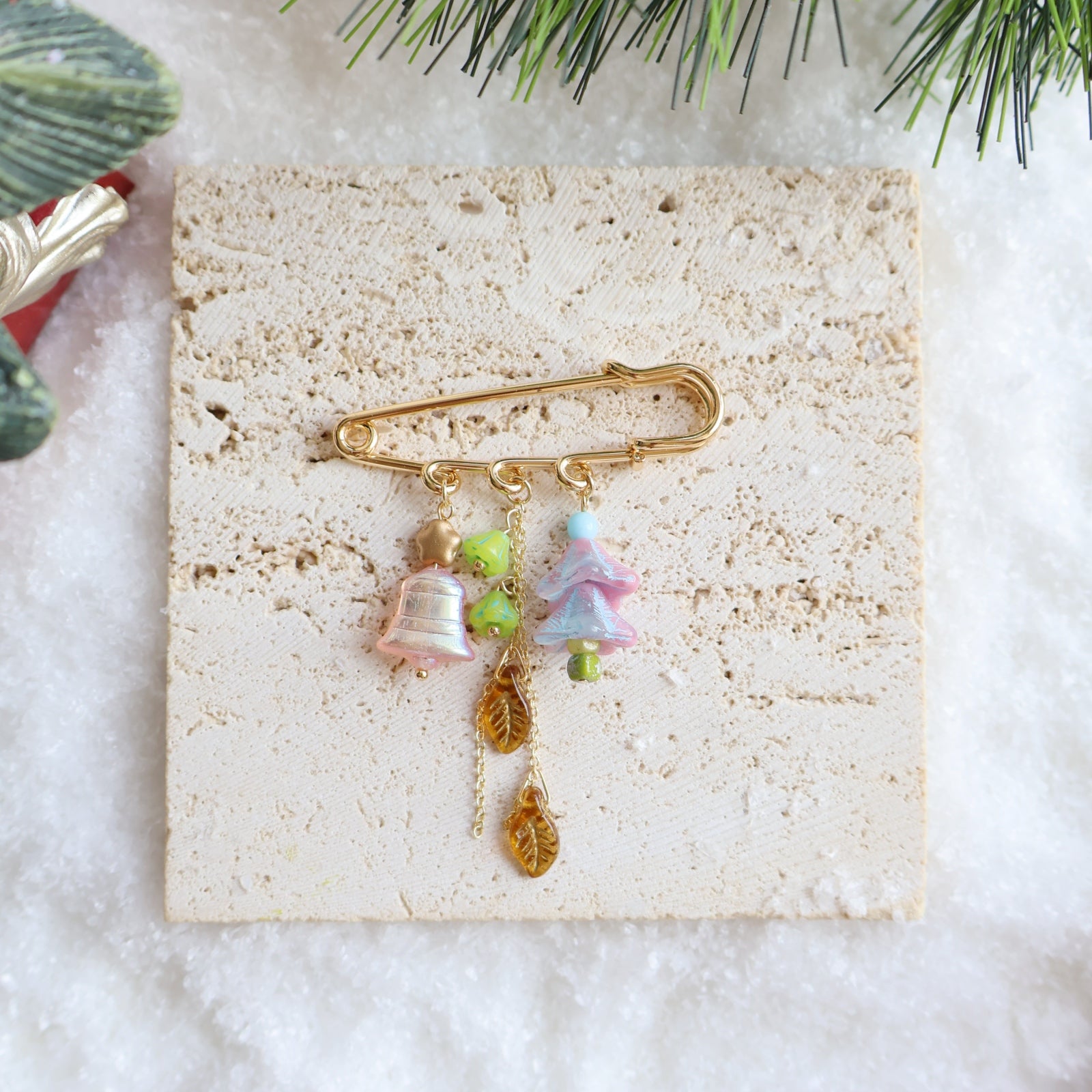 Decorative brooch with bell and tree charms on a textured card with Christmas decorations.