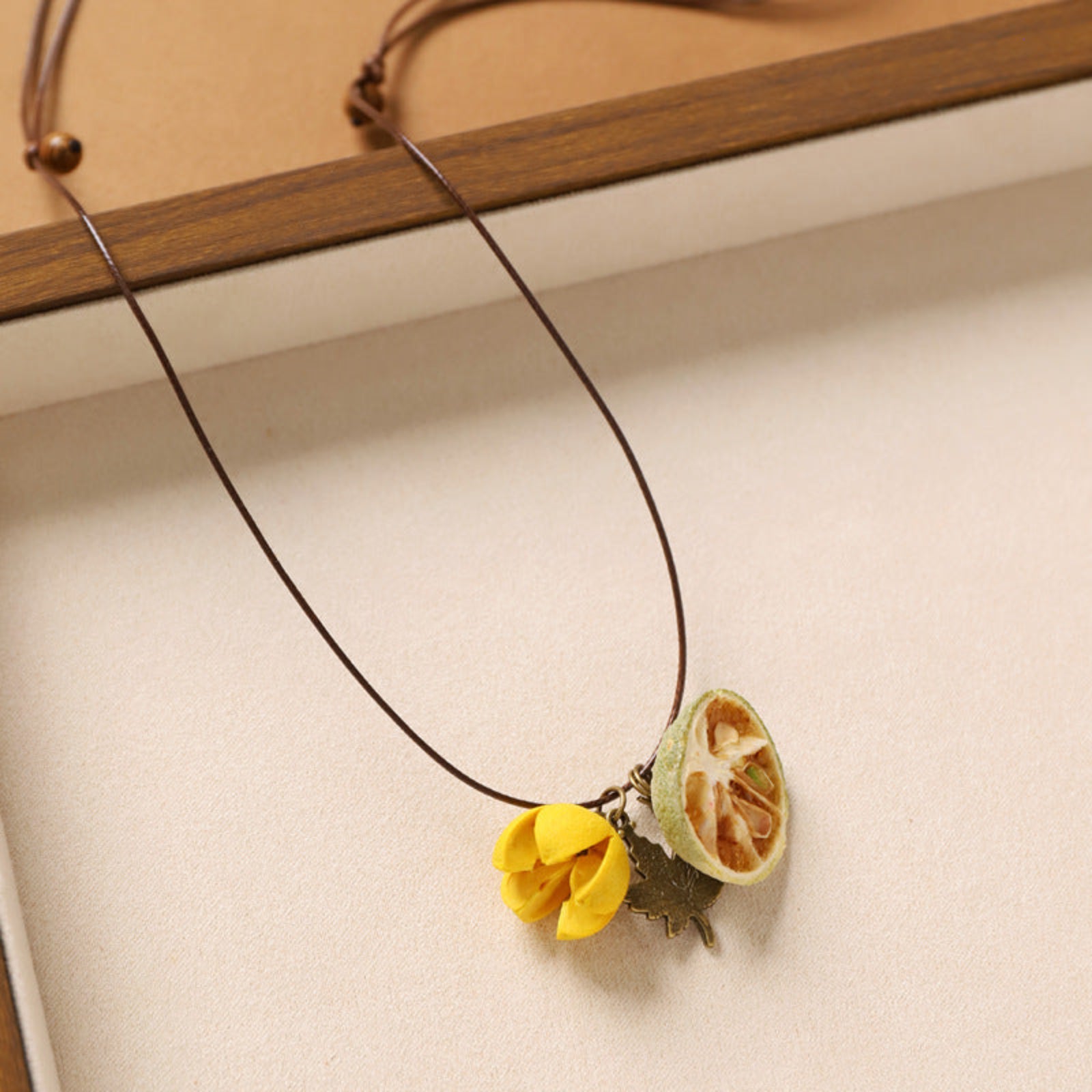 Necklace with a yellow flower and green leaf pendant on a beige background
