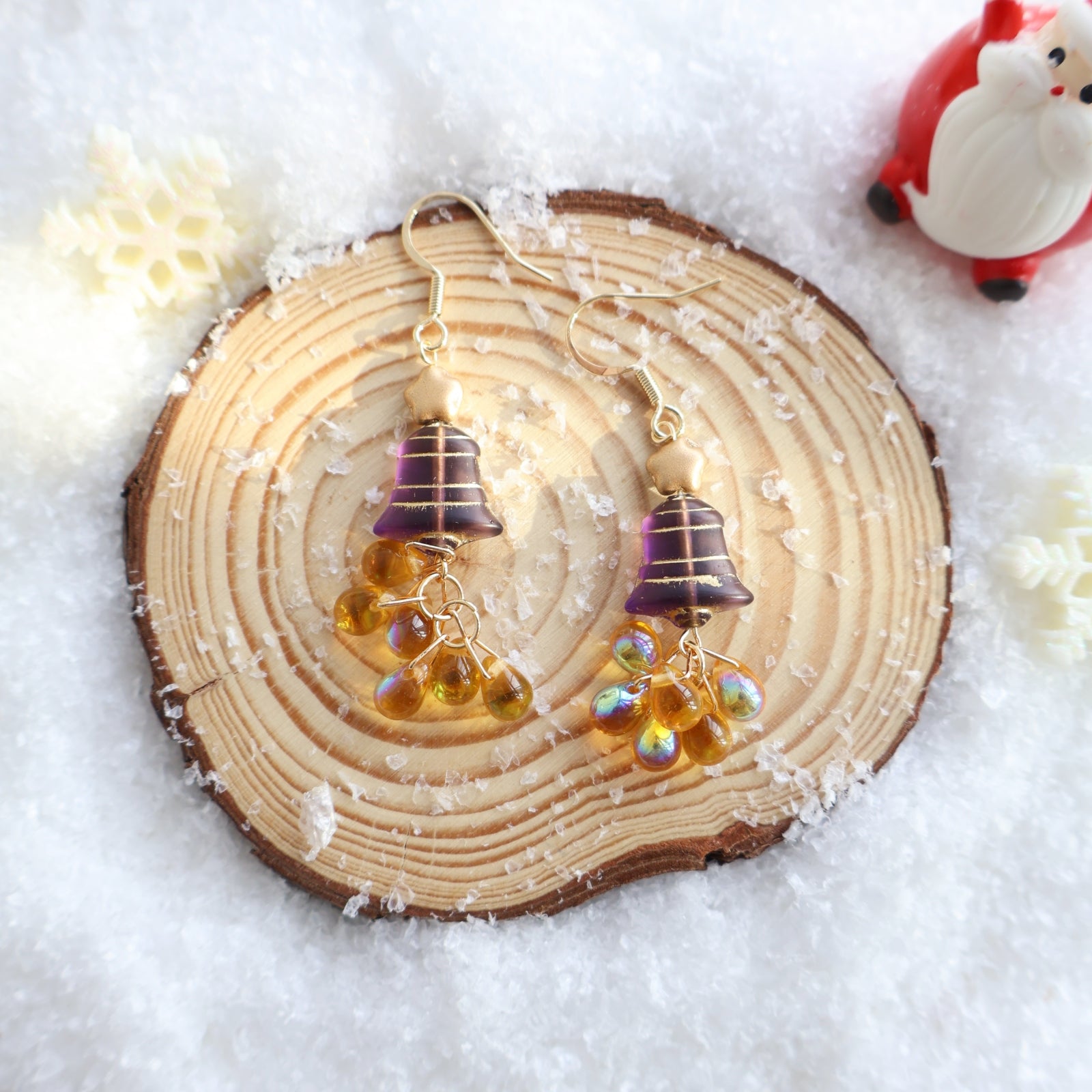 Pair of earrings with purple and gold elements on a wooden slice with snow-like background