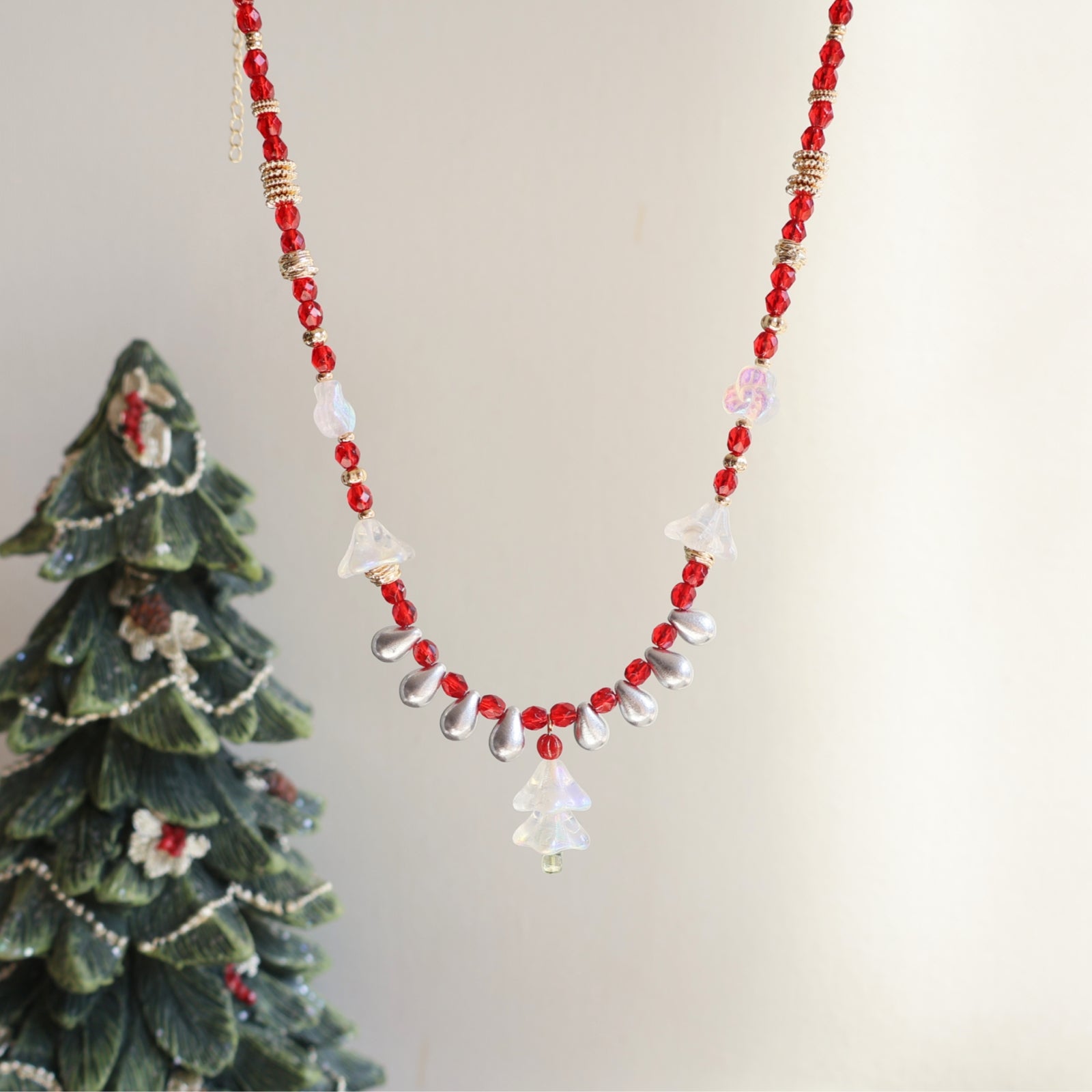 Beaded necklace with red and clear beads next to a small Christmas tree figurine on a light background