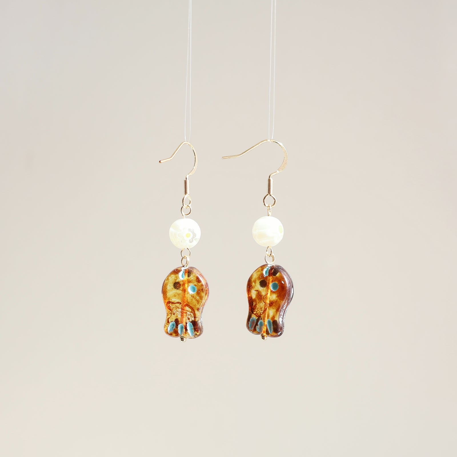 Pair of earrings with tortoiseshell design and pearl-like beads on a beige background