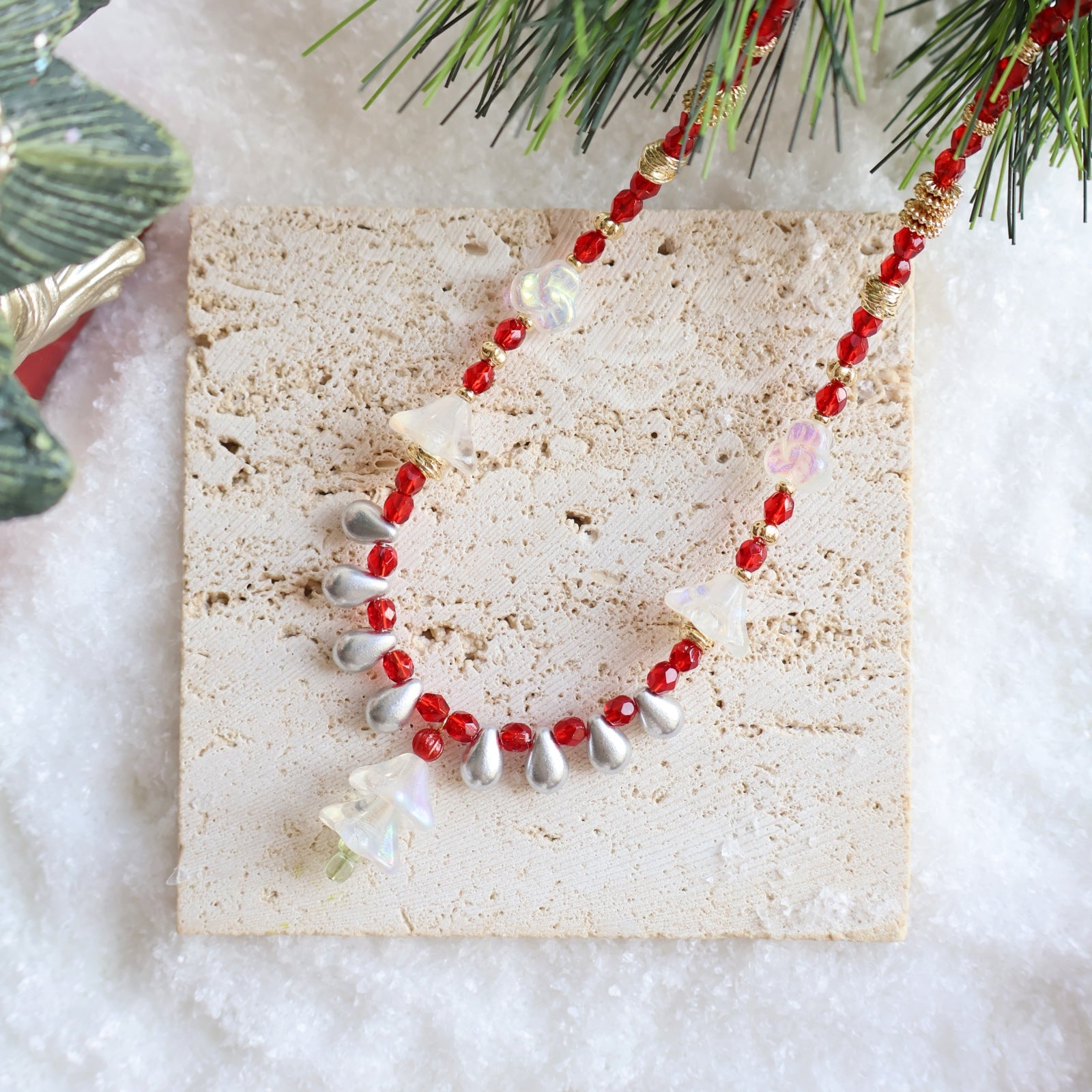 Necklace with red and silver beads on a textured card with Christmas decorations.