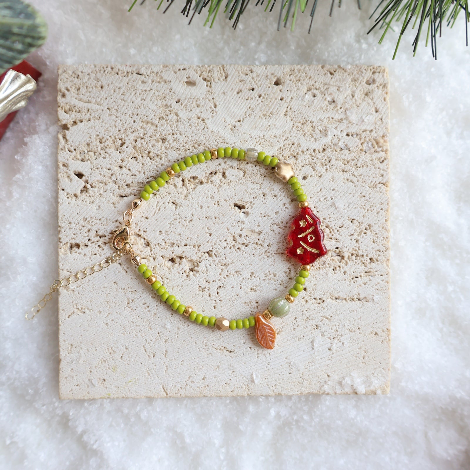 Bracelet with green beads and a red charm on a textured card with a snowy background
