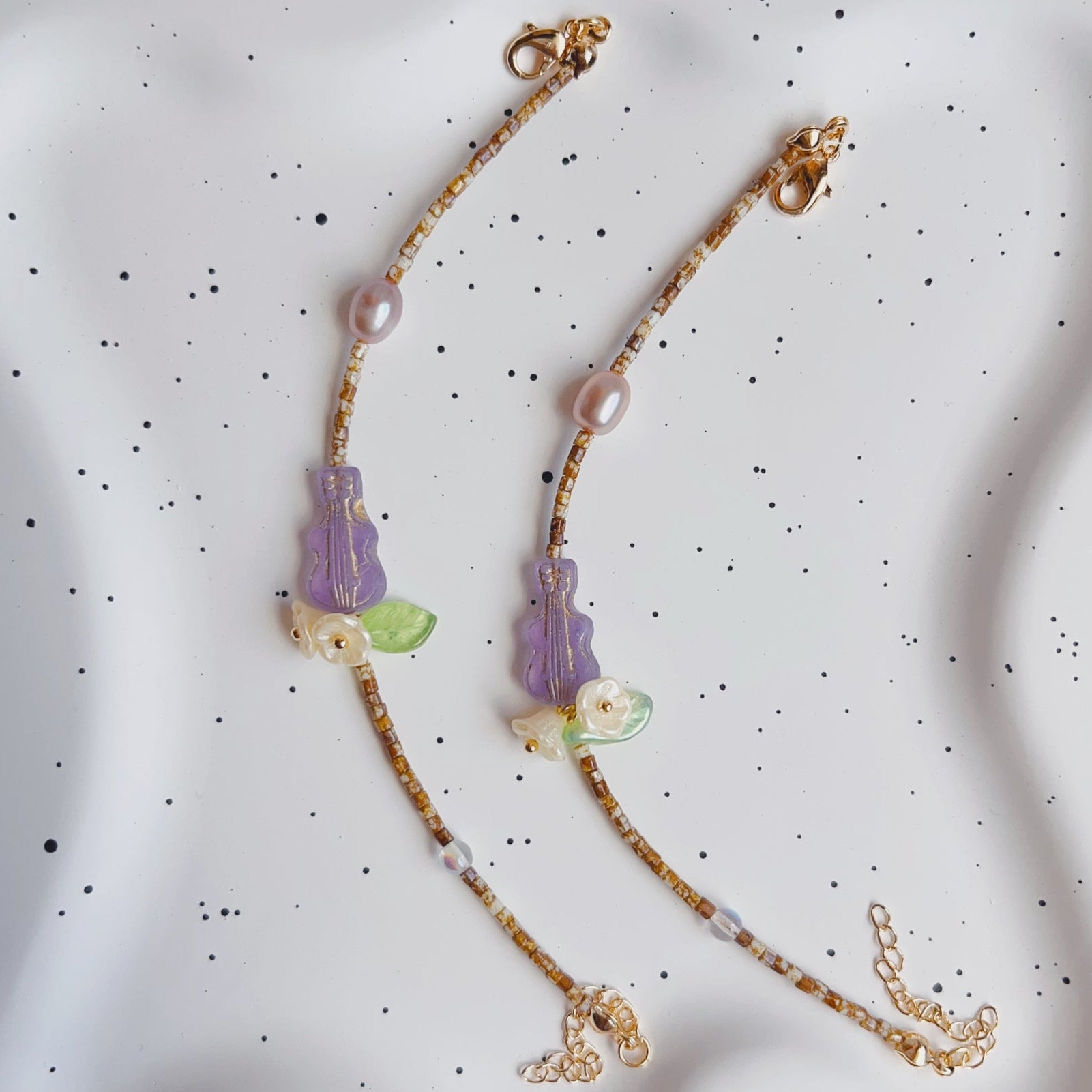 Necklace with purple pendants and gold chain on a textured white background