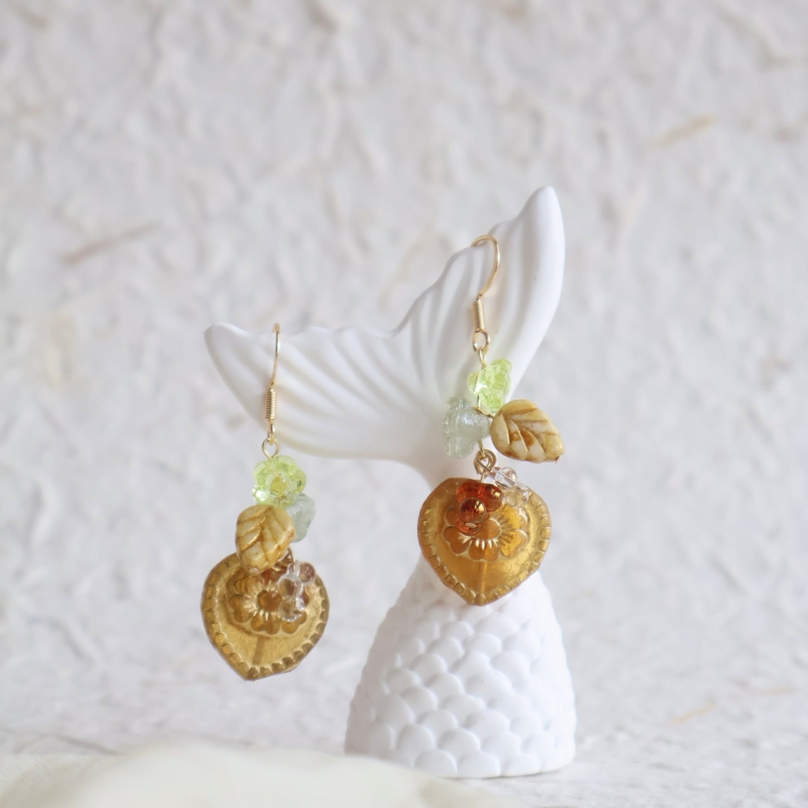 Gold and green leaf-themed earrings on a white stand with a white background