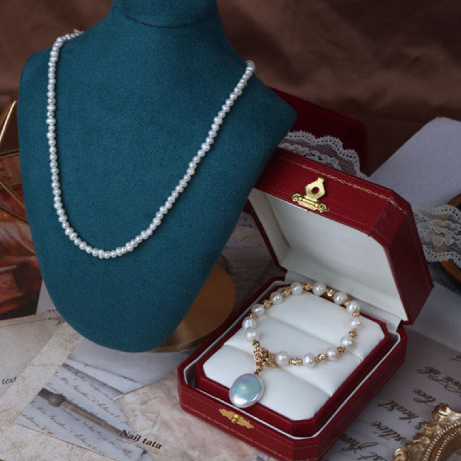 Pearl necklace displayed on a mannequin bust and in an open jewelry box with vintage papers in the background.