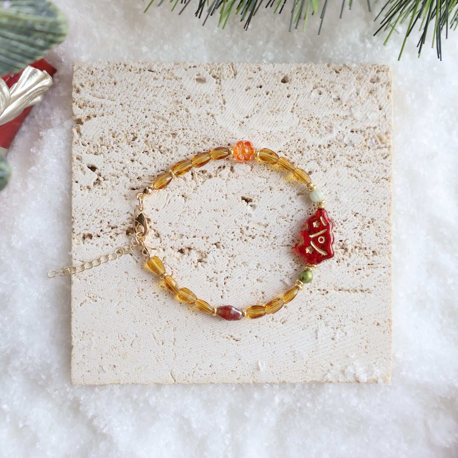 Beaded bracelet with red and orange accents on a textured beige card with a snowy background