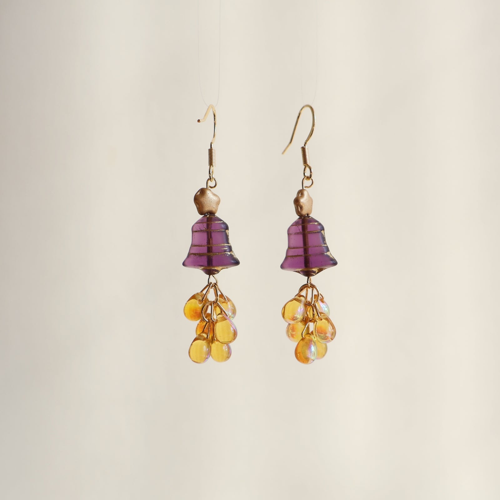 Pair of earrings with purple and yellow beads on a beige background