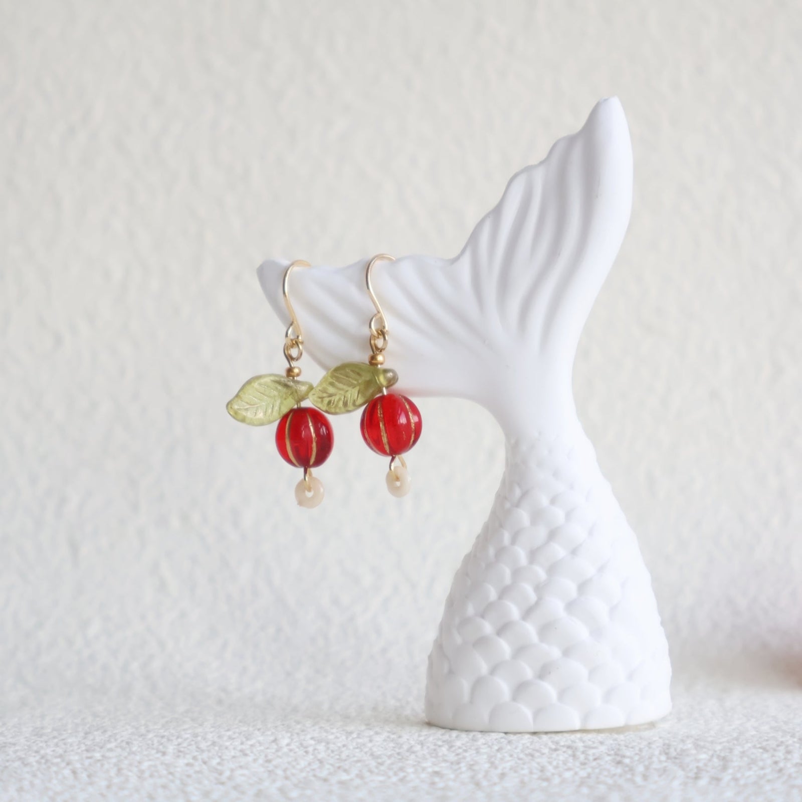 Earrings with red berries and green leaves on a white decorative stand against a light gray background