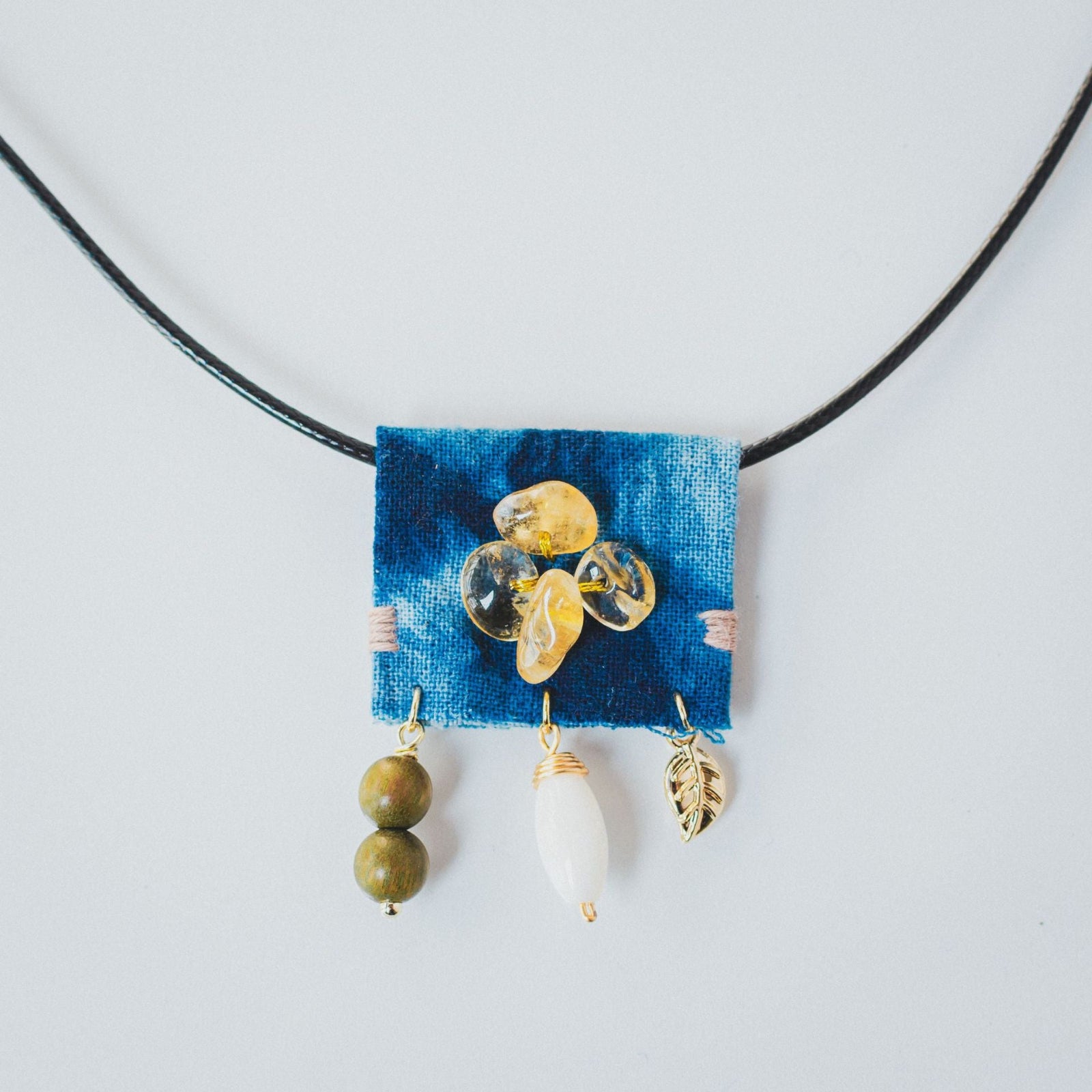 Necklace with a blue fabric patch and various beads on a white background