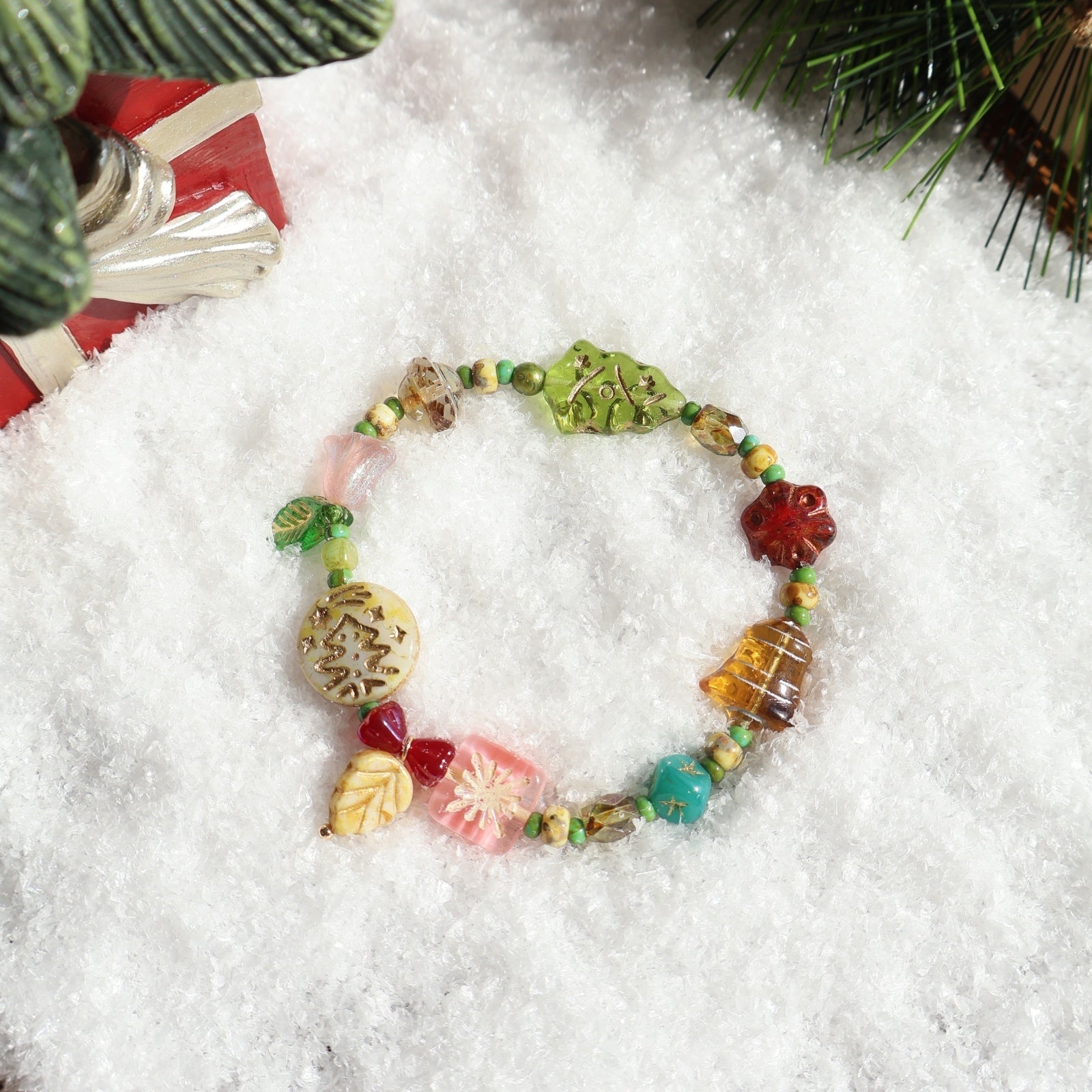 Colorful beaded bracelet on a snowy surface with Christmas decorations.