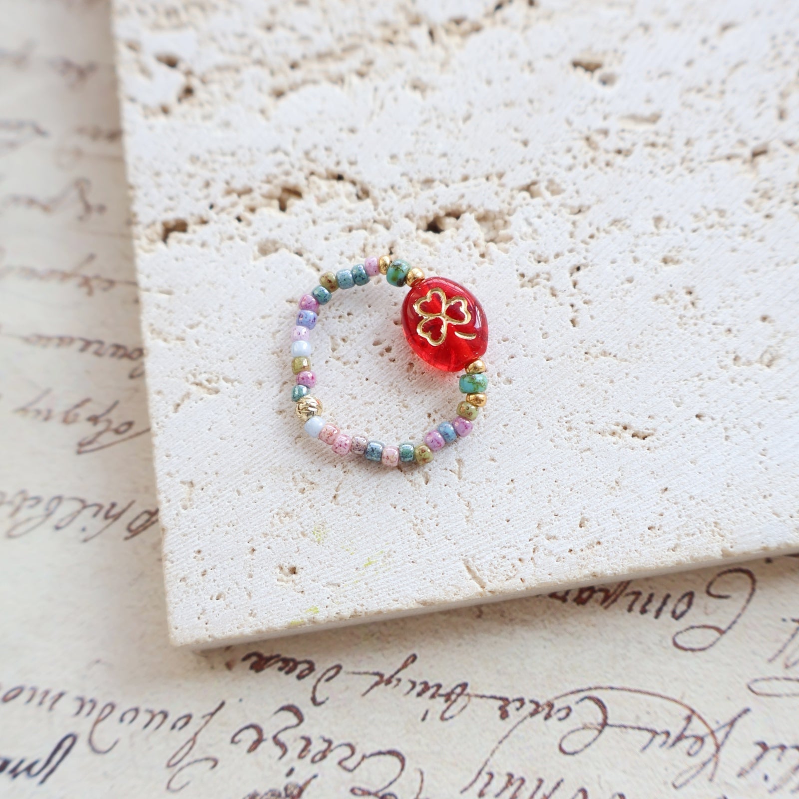 Beaded ring with a red flower charm on a textured surface with cursive text.