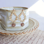 Gold earrings with pink gemstones on a white teacup and saucer.