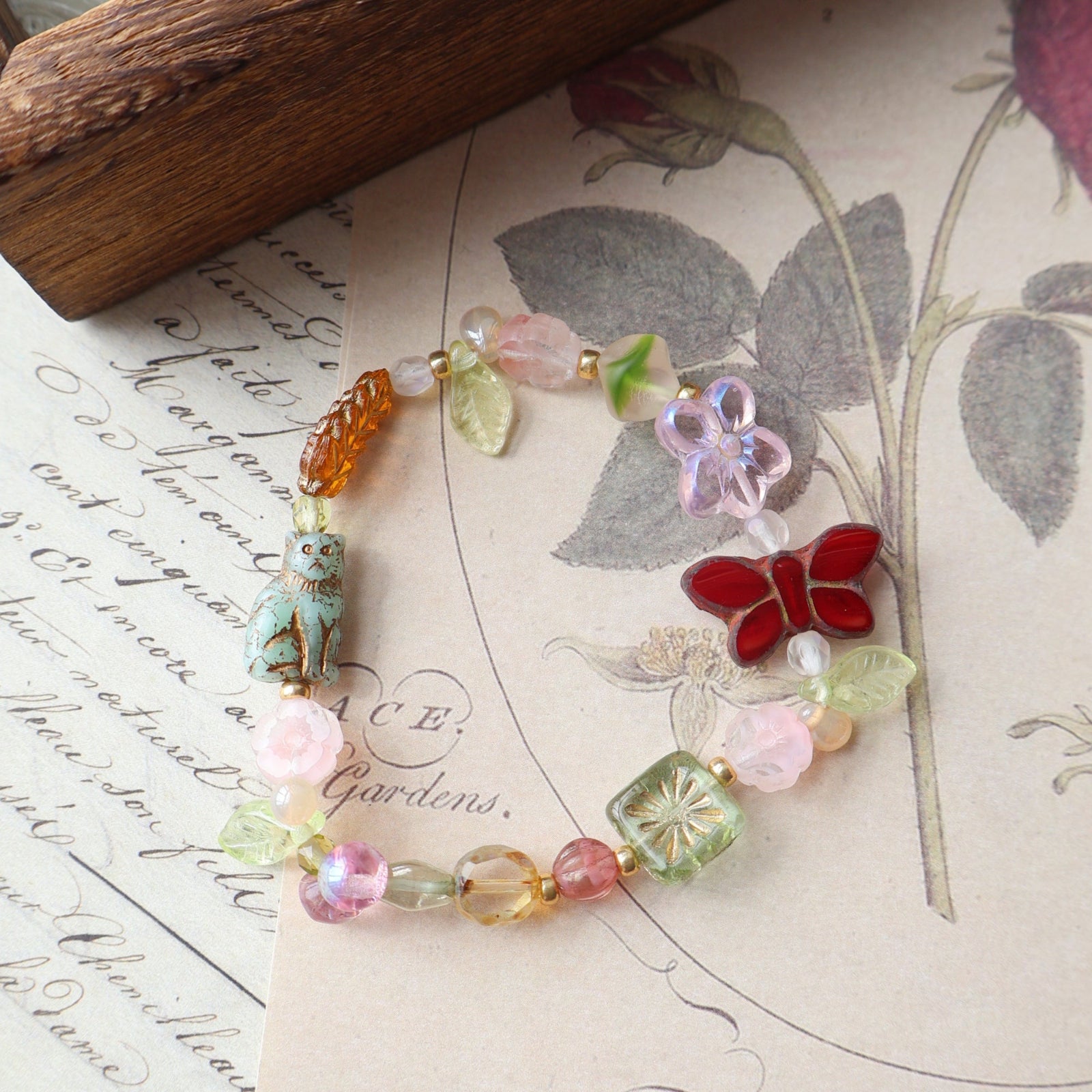 Colorful beaded bracelet with a butterfly charm on an old letter with botanical illustrations.