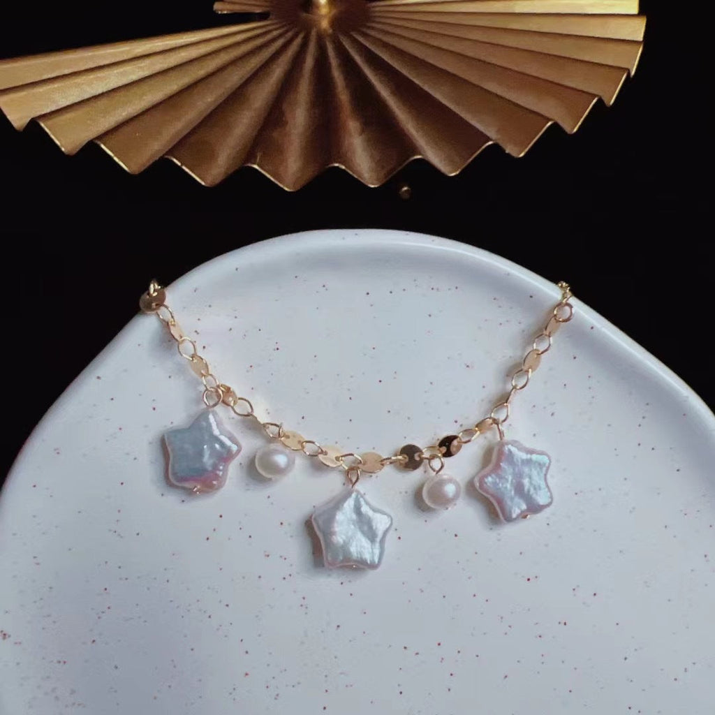 Gold bracelet with star-shaped charms on a white plate with a gold decorative object in the background.