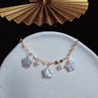 Gold bracelet with star-shaped charms on a white plate with a gold decorative object in the background.