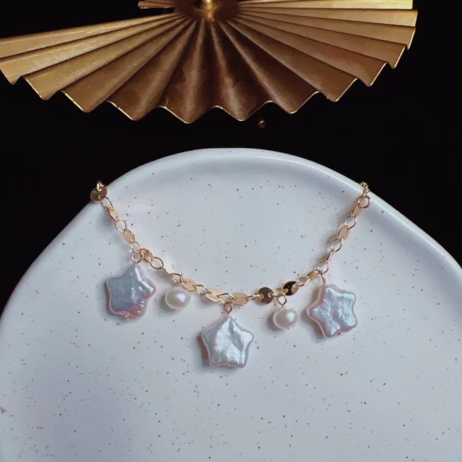 Gold bracelet with star-shaped charms on a white plate with a gold decorative object in the background.