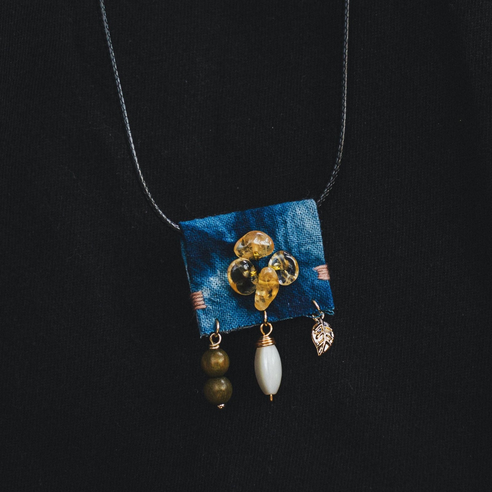 Necklace with blue fabric pendant and beads on a black background