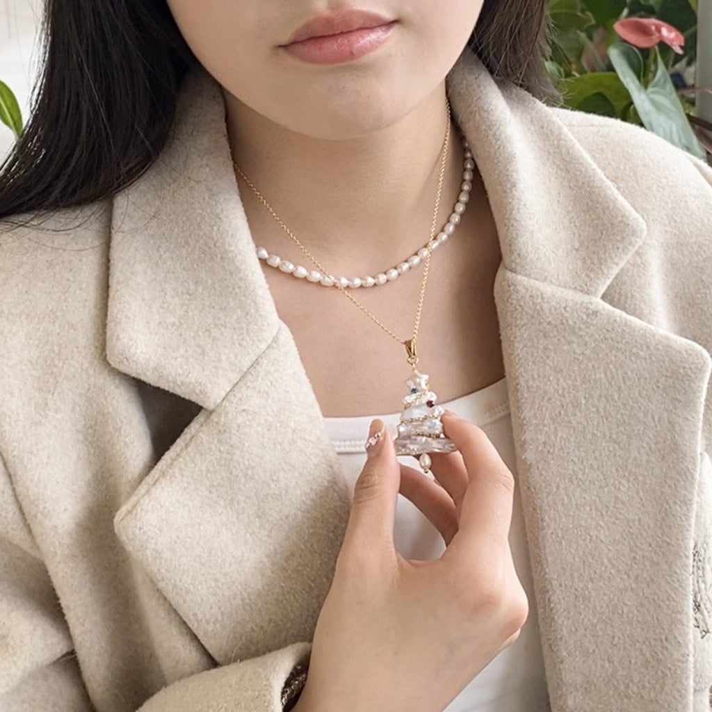 Person wearing a pearl necklace and holding a small decorative object, with a neutral background.