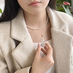 Person wearing a pearl necklace and holding a small decorative object, with a neutral background.