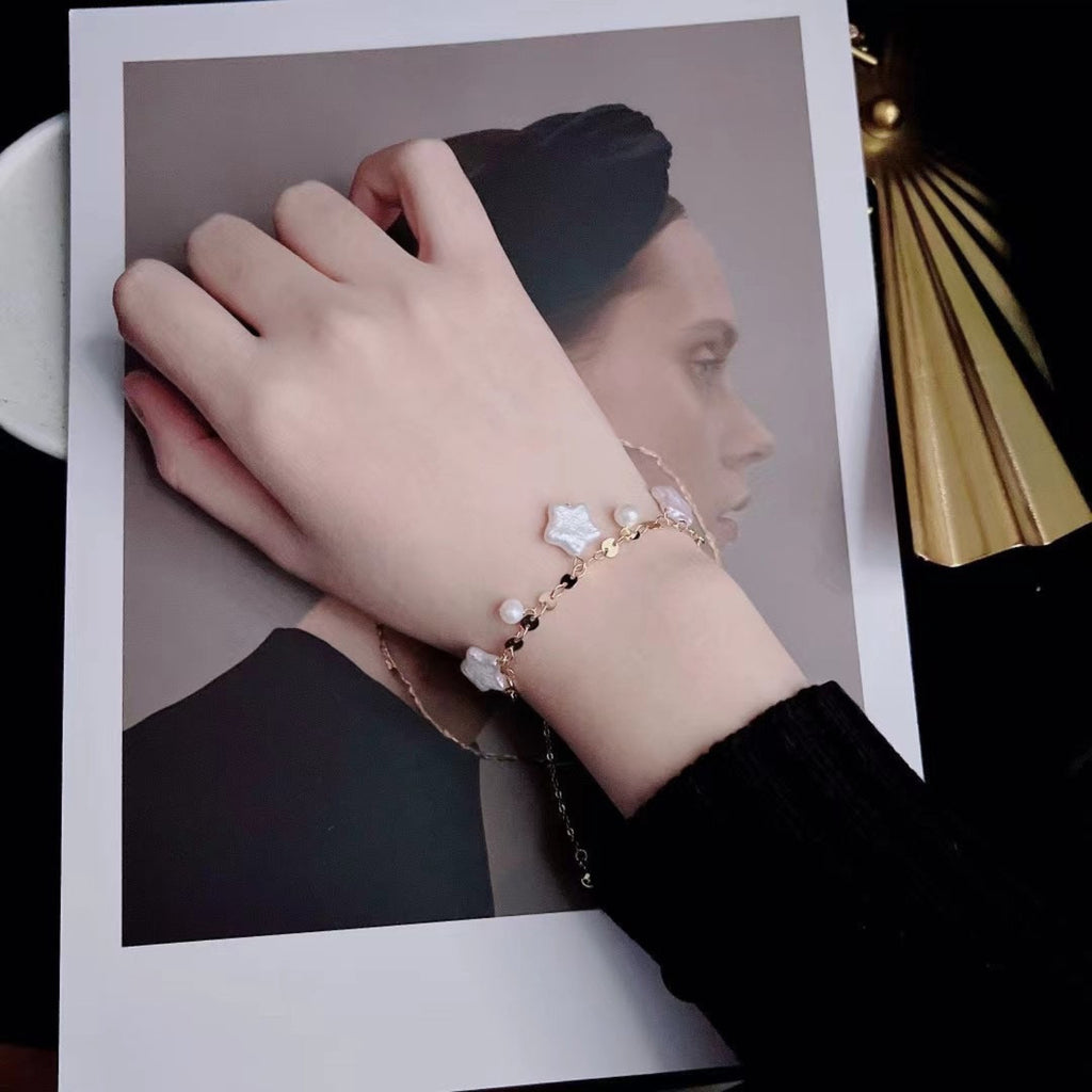Hand wearing a bracelet with star-shaped charms on a plain background