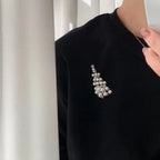 Black sweater with a decorative brooch against a neutral background