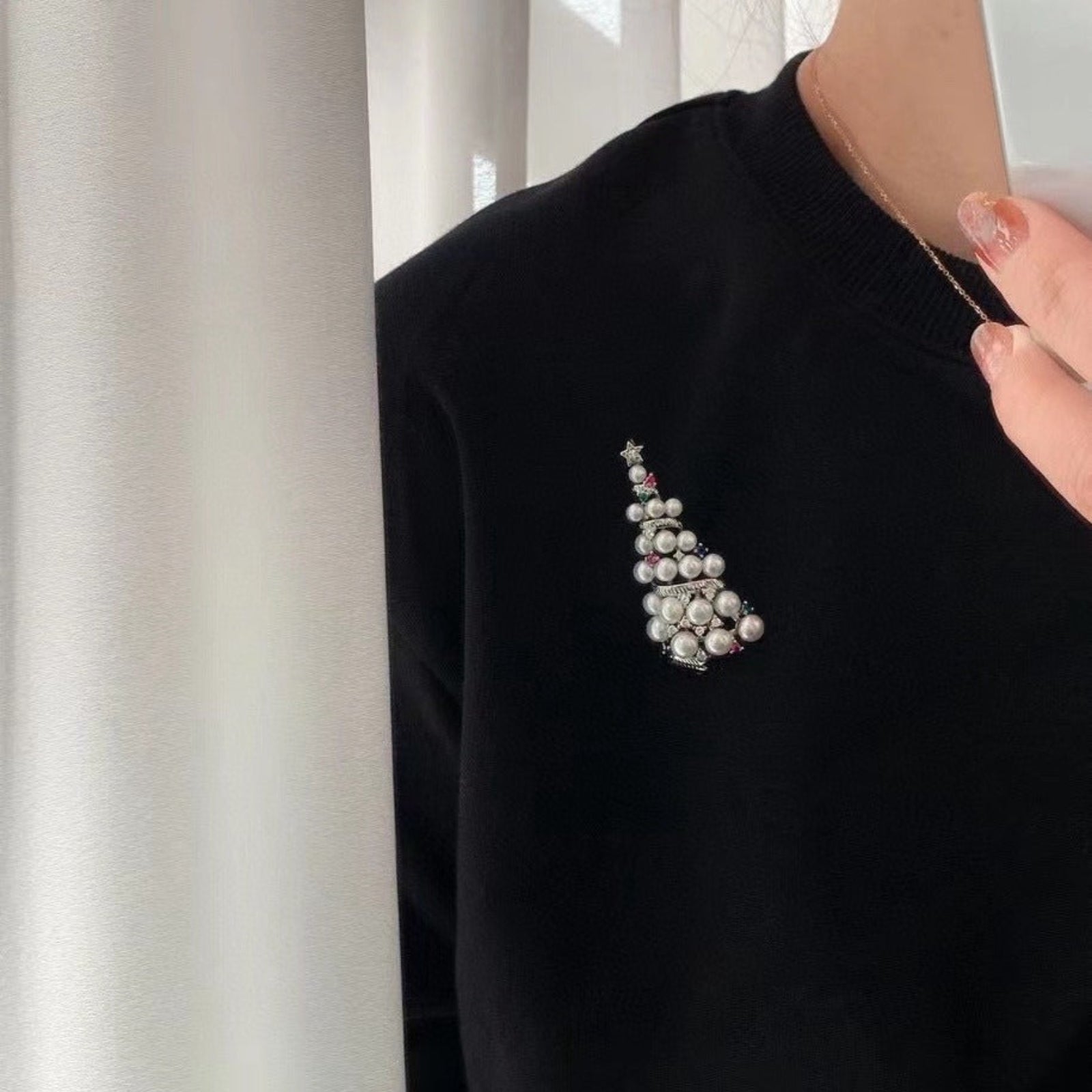 Black sweater with a decorative brooch against a neutral background